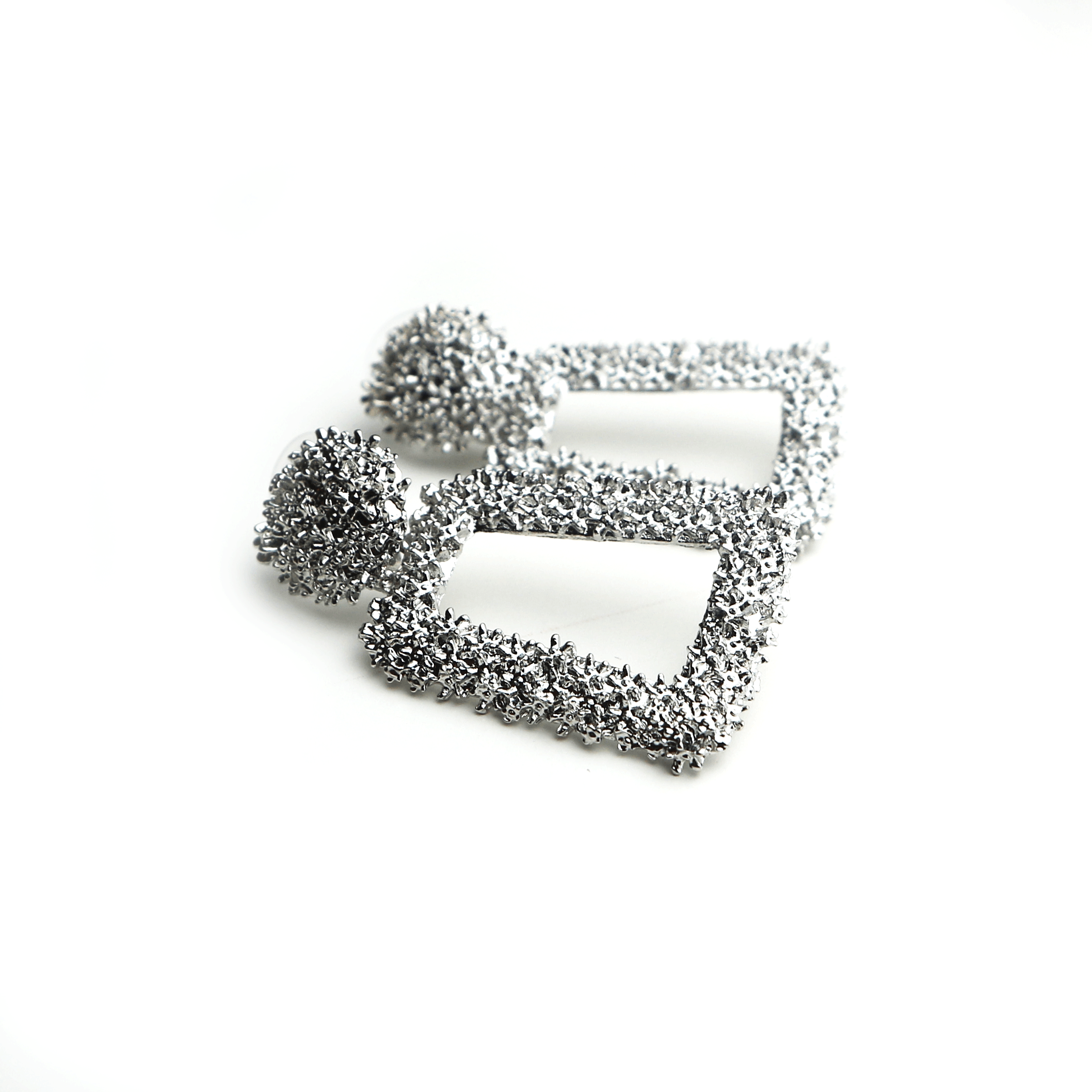 Pair of silver square-shaped earrings with textured, clustered ball designs on the top portion, resting on a plain white surface.