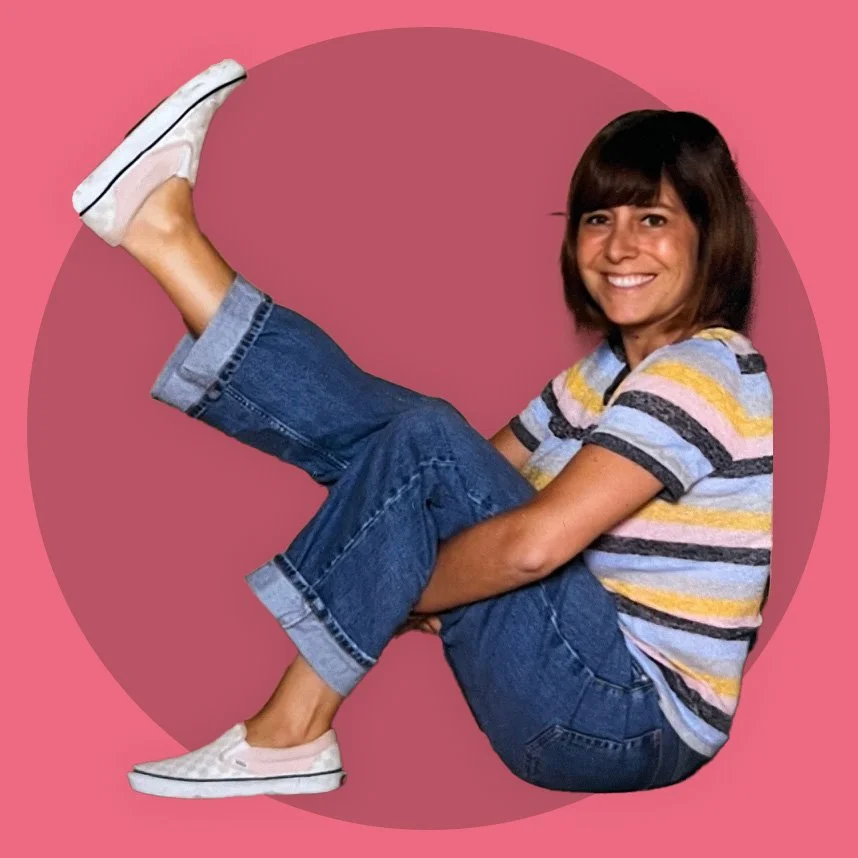 Junge Frau sitzt auf dem Boden vor einem pinken Hintergrund, trägt Jeans, T-Shirt mit Streifen, Turnschuhe, lächelt.