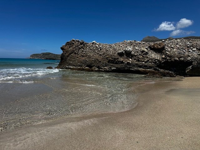 Pink sand blending into crystal-clear water near rock edges at Falassarna Beach