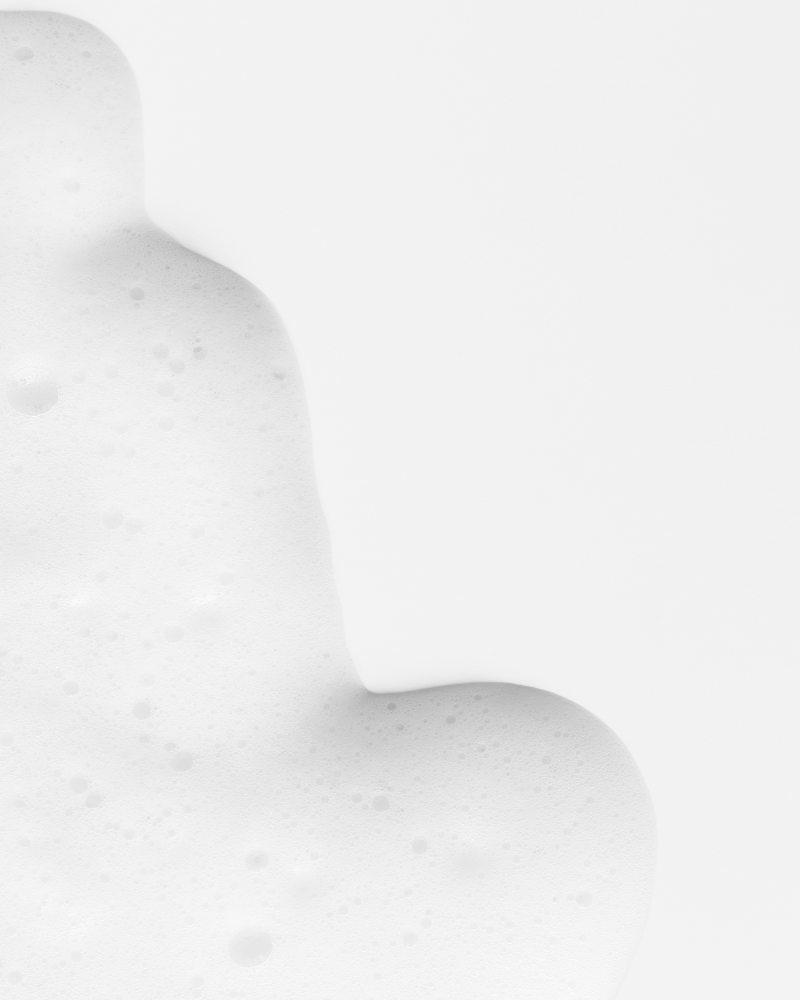 Close-up of soft, delicate foam and bubbles from natural soap lather on a clean white background, capturing a gentle and minimal cleansing texture.
