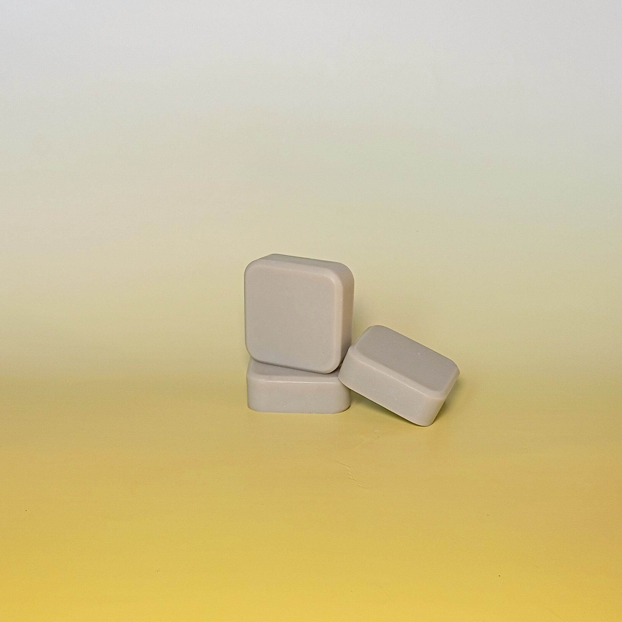Three bars of handmade soap with green colour, stacked on a gradient yellow background.