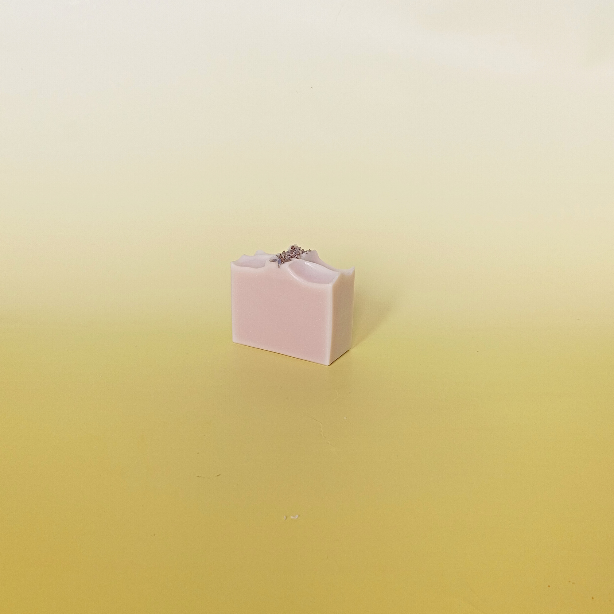 Lavender soap bar with buds on top, on a soft yellow background.