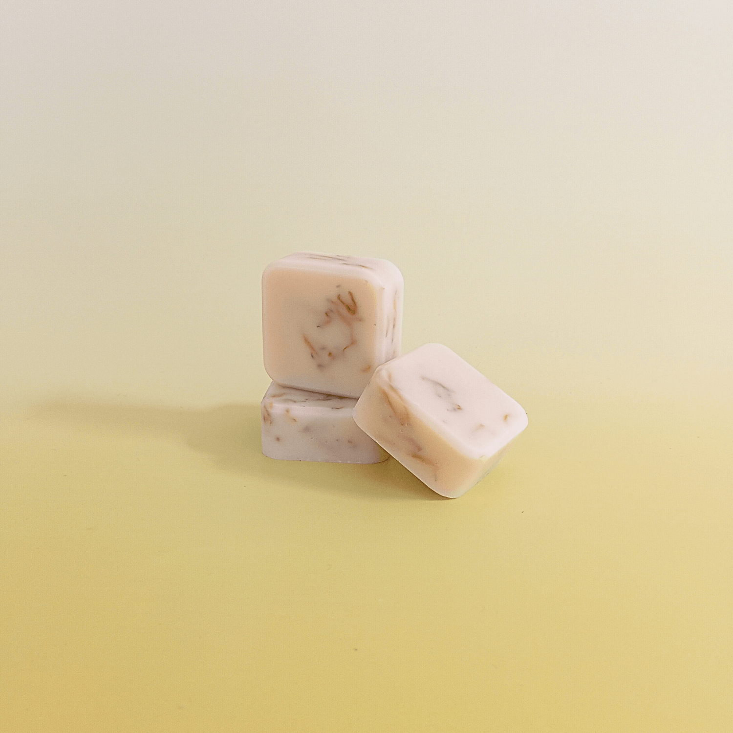 Three handmade soap bars in soft cream tones with calendula petals, crafted with calendula-infused oil and citrus essential oils. Stacked on a pale yellow background.