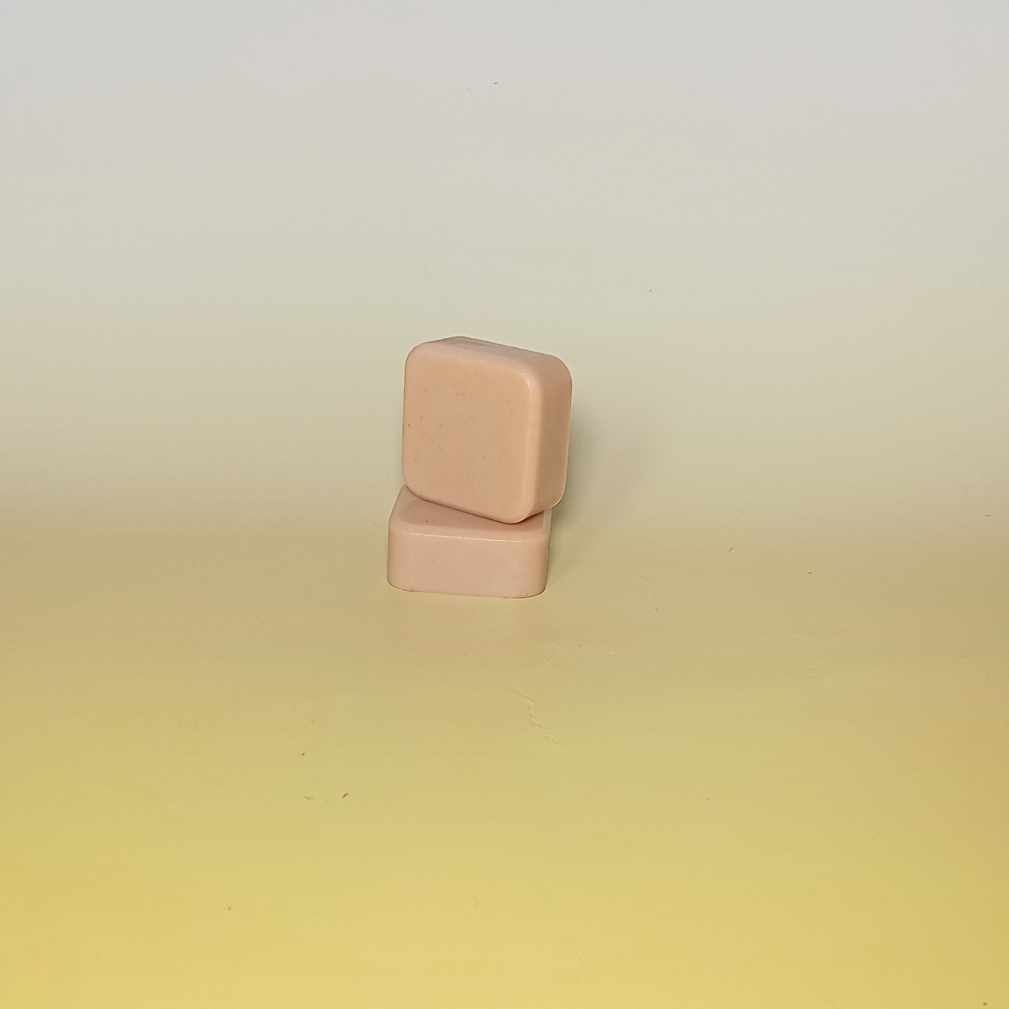 Two handmade soap bars in soft orange tones with orange peel exfoliant, scented with orange and geranium essential oils. Stacked on a pale yellow background.