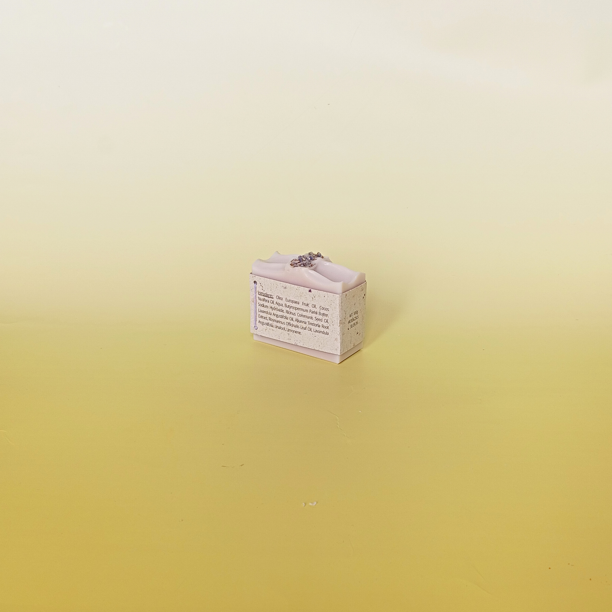 Lavender soap bar wrapped in grass paper sleeve with buds on top, on a soft yellow background_back