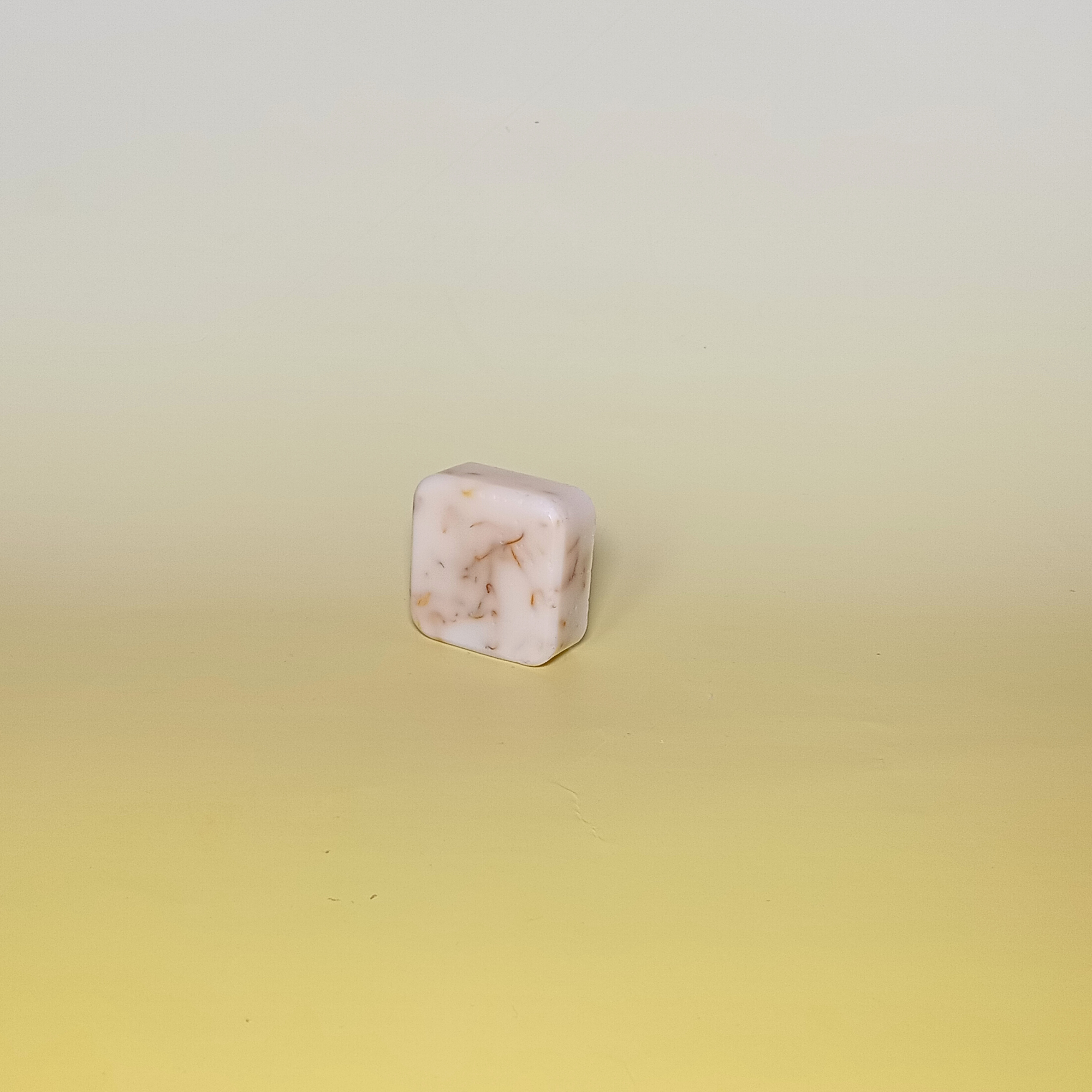 Handmade soap bar in soft cream tone with calendula petals, made with calendula-infused oil and citrus essential oils. Shown on a pale yellow background.