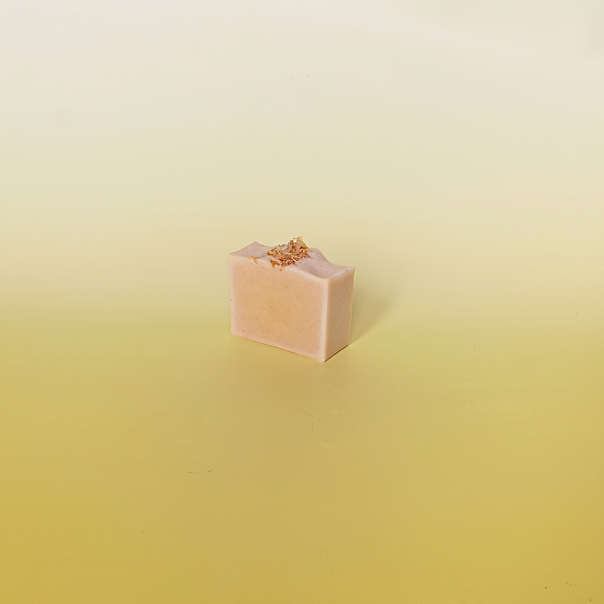 Handmade natural soap bar in warm golden tones with calendula petals, crafted with turmeric and citrus essential oils. Displayed on a soft yellow background.