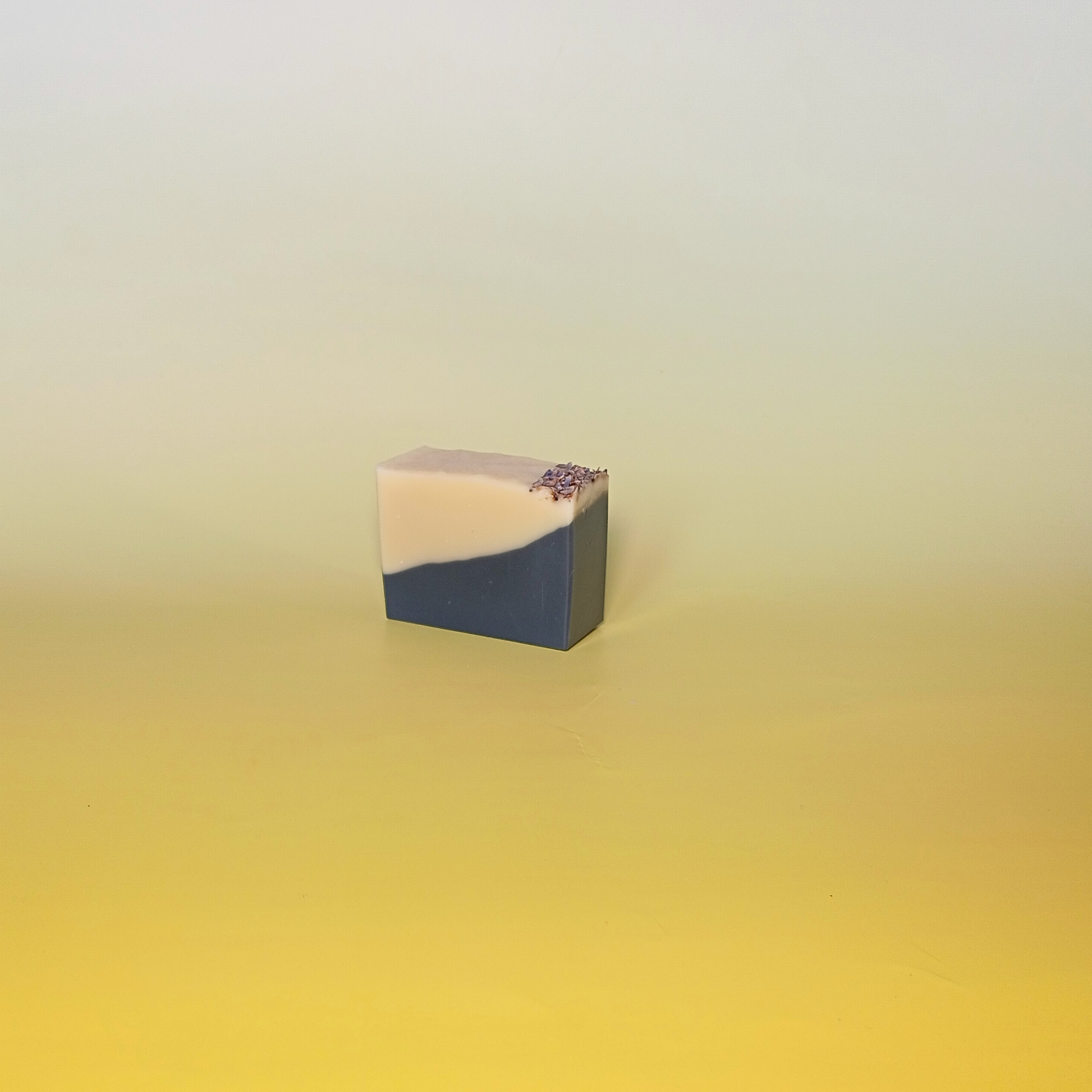 One soap bar with bold black and cream design, crafted with charcoal powder and scented with orange, patchouli, and lavender essential oils. Stacked on a soft yellow background.