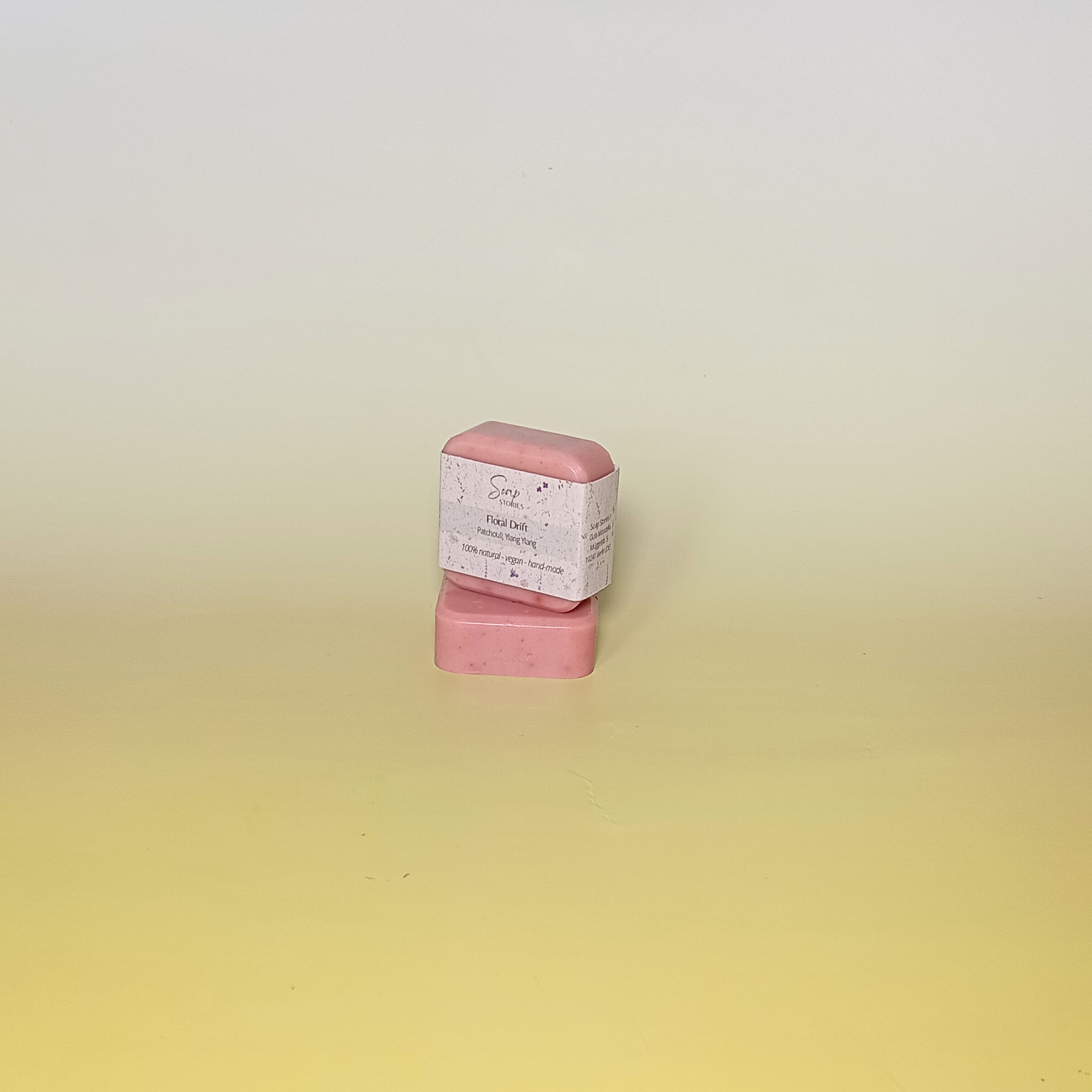 Pink soap bar wrapped in grass paper sleeve, on a soft yellow background.