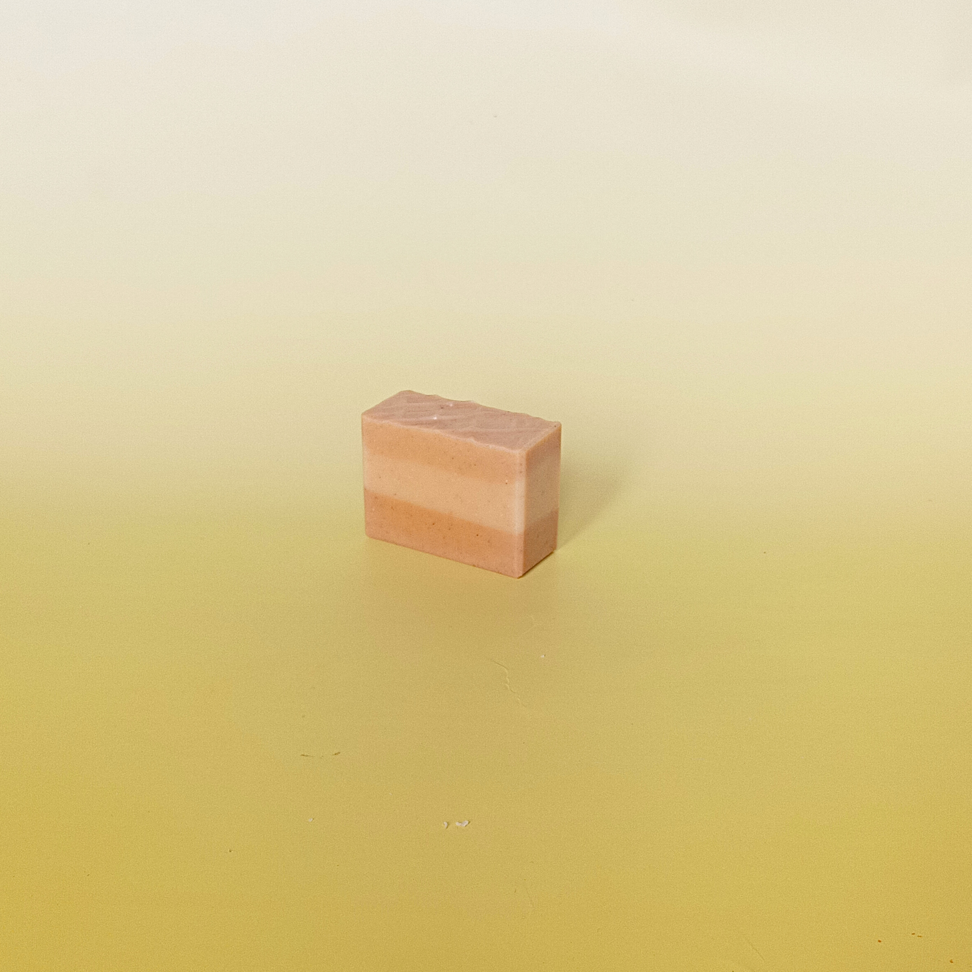 Handmade natural soap bar in warm golden tones with calendula petals, crafted with turmeric and citrus essential oils. Displayed on a soft yellow background.