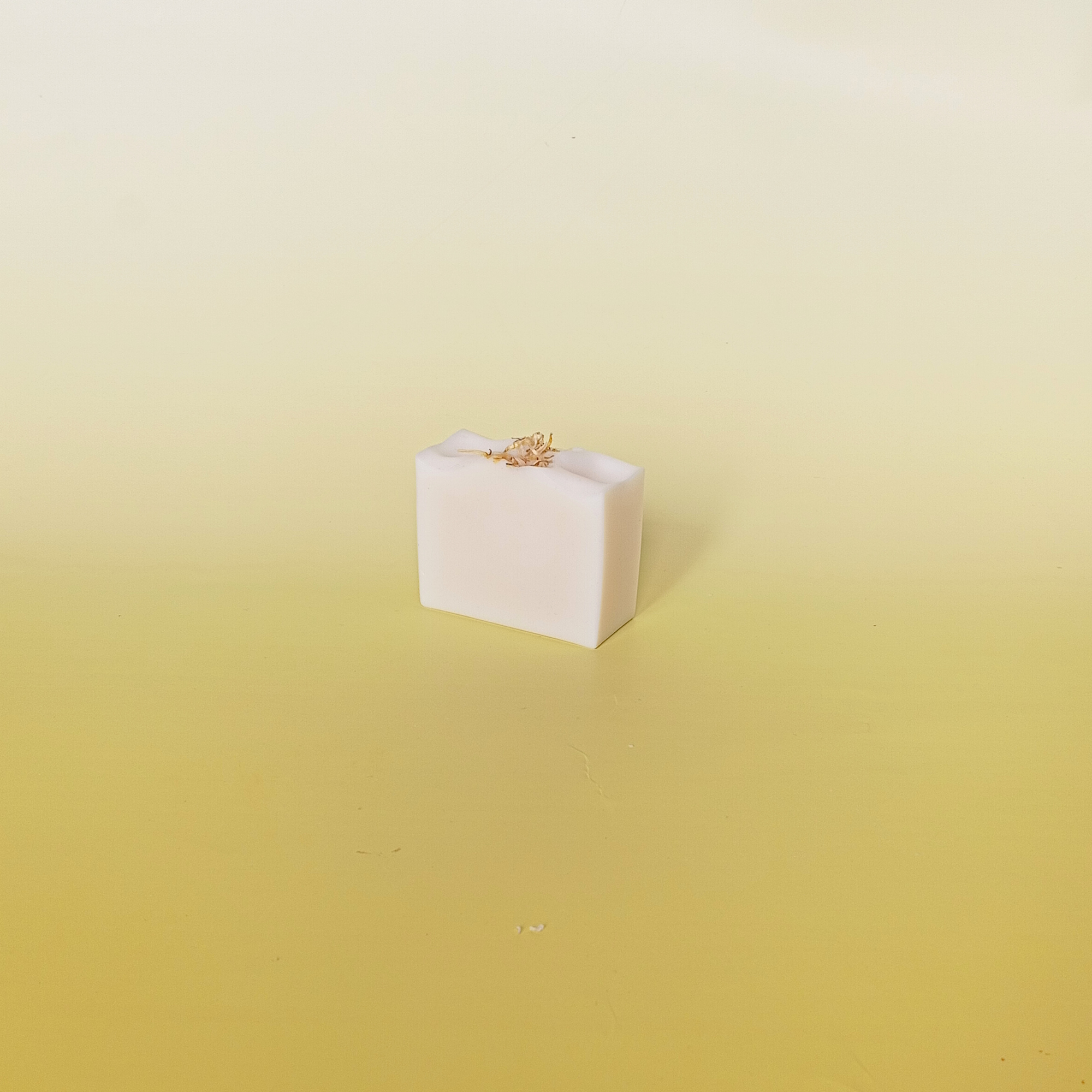 Handmade natural soap bar in soft ivory tone with delicate dried petals on top, displayed on a pale yellow gradient background, showcasing minimal and gentle design.