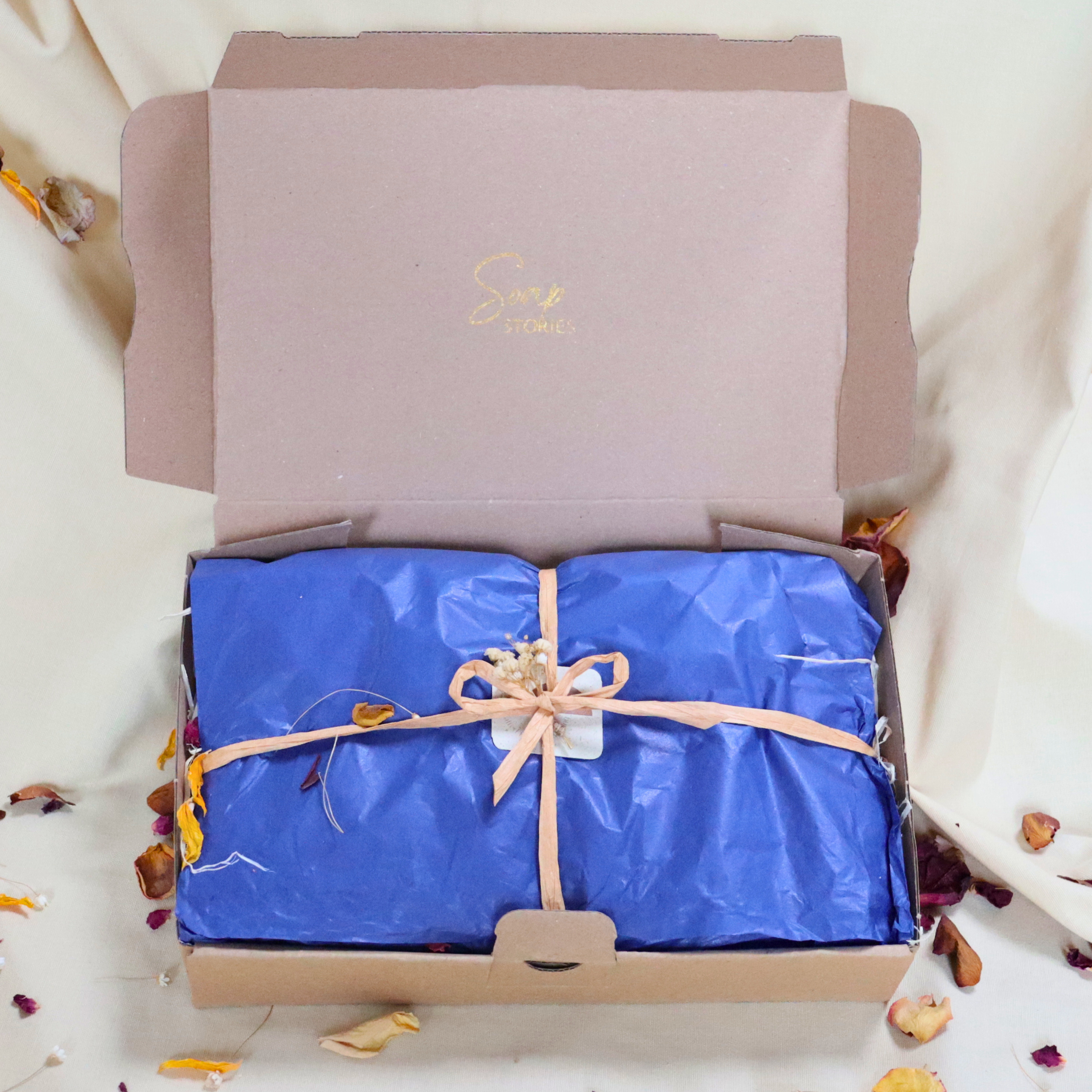 Eco-friendly gift box with handmade soaps wrapped in tissue and twine, decorated with dried flowers and leaves.”
