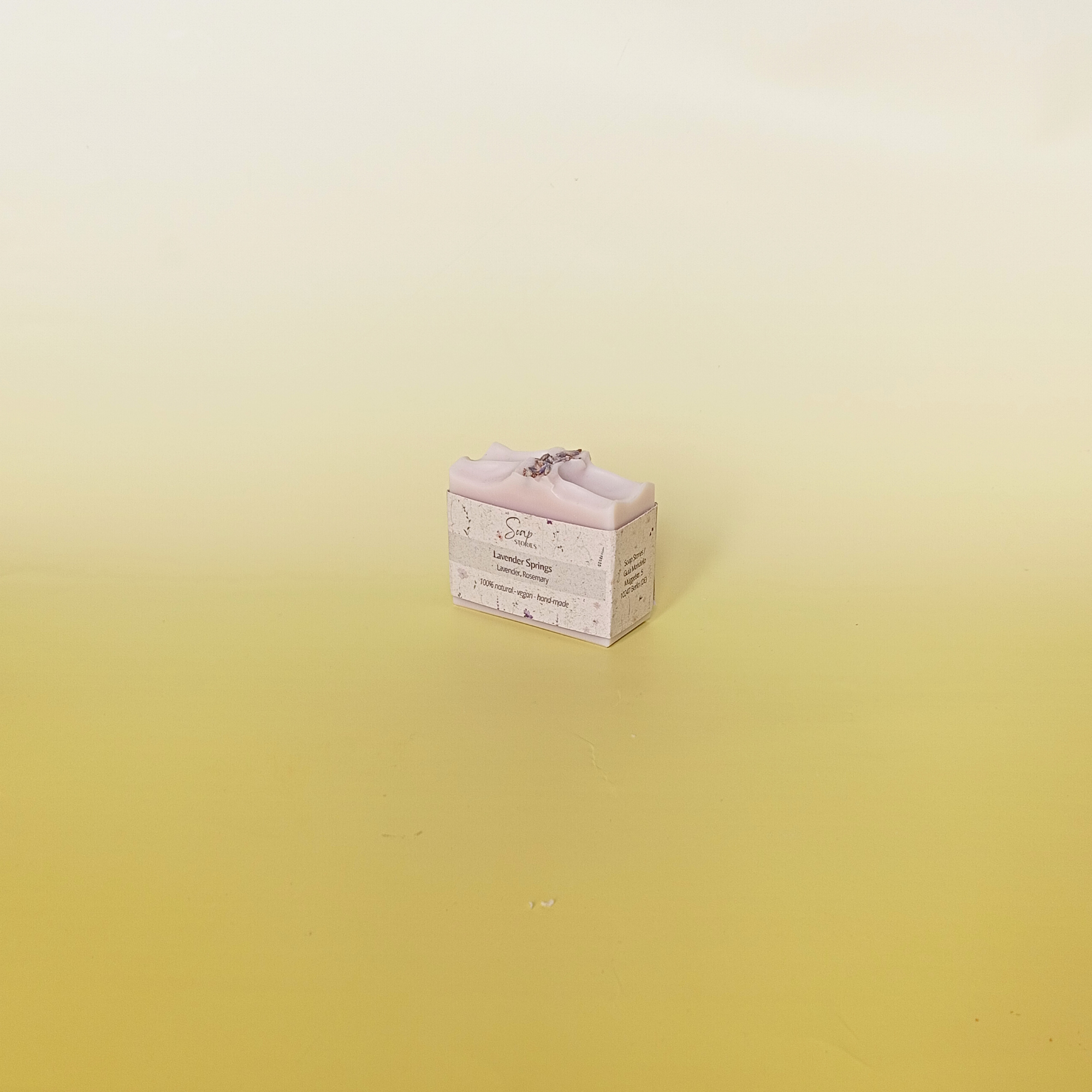 Lavender soap bar wrapped in grass paper sleeve with buds on top, on a soft yellow background.