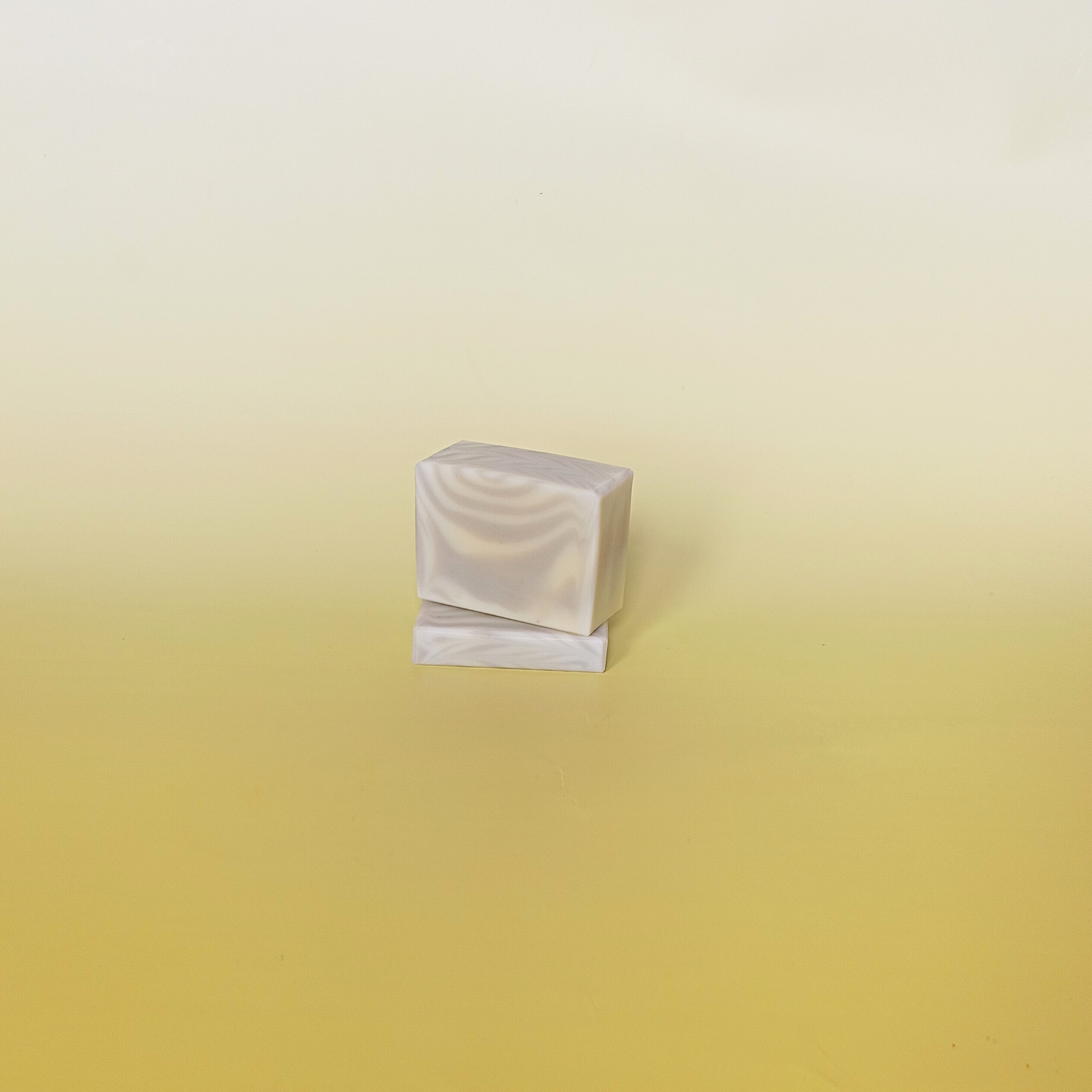 Two bars of handmade soap with green and cream swirls stacked on a gradient yellow background.