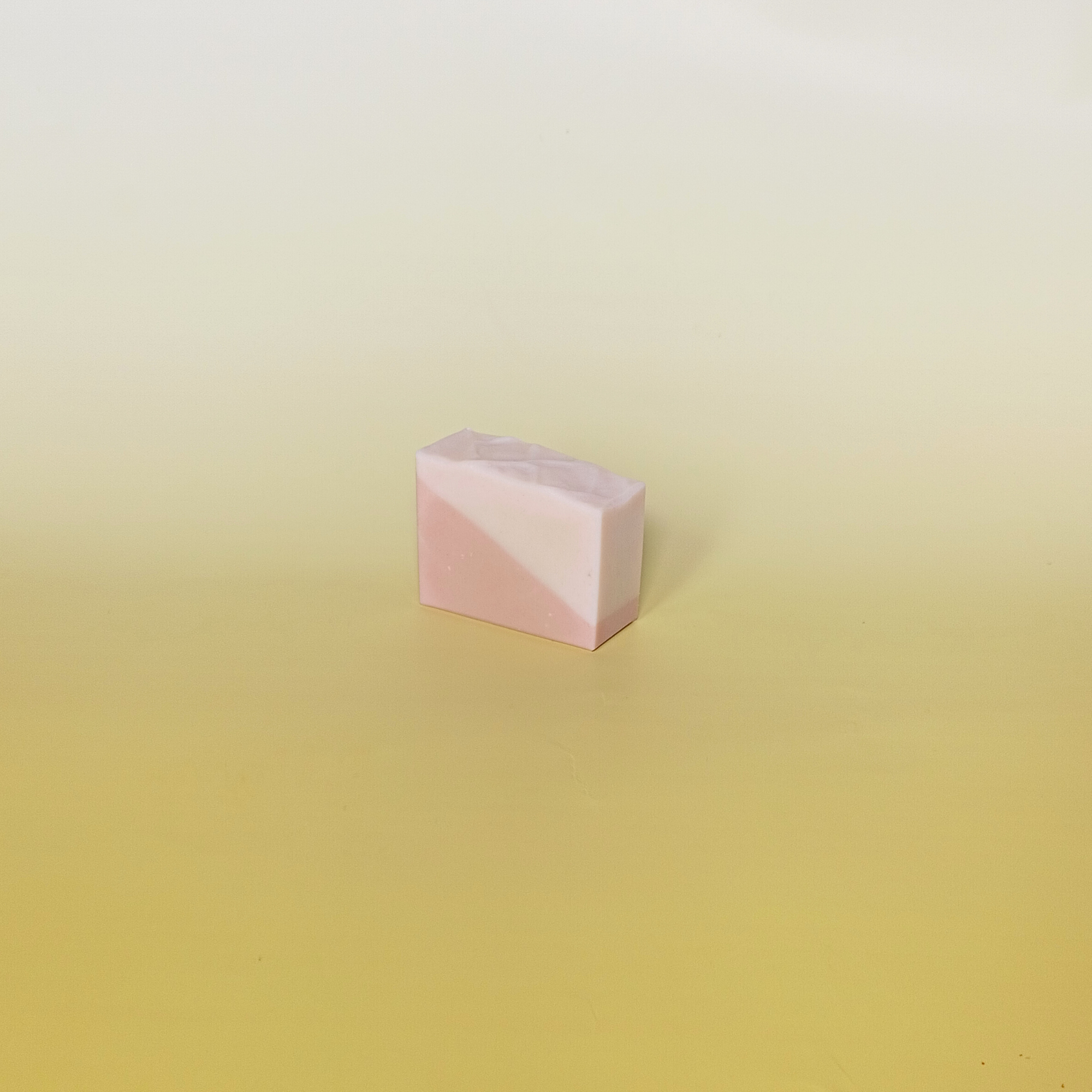 Single handmade soap bar with pink and cream diagonal pattern on a soft yellow background.