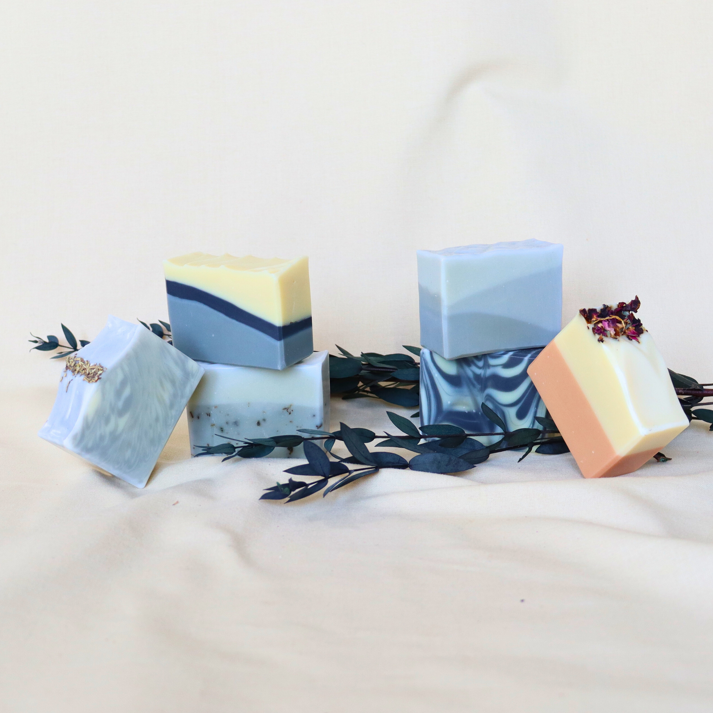 Blue and cream natural vegan soaps arranged with dark eucalyptus leaves on soft beige backdrop.