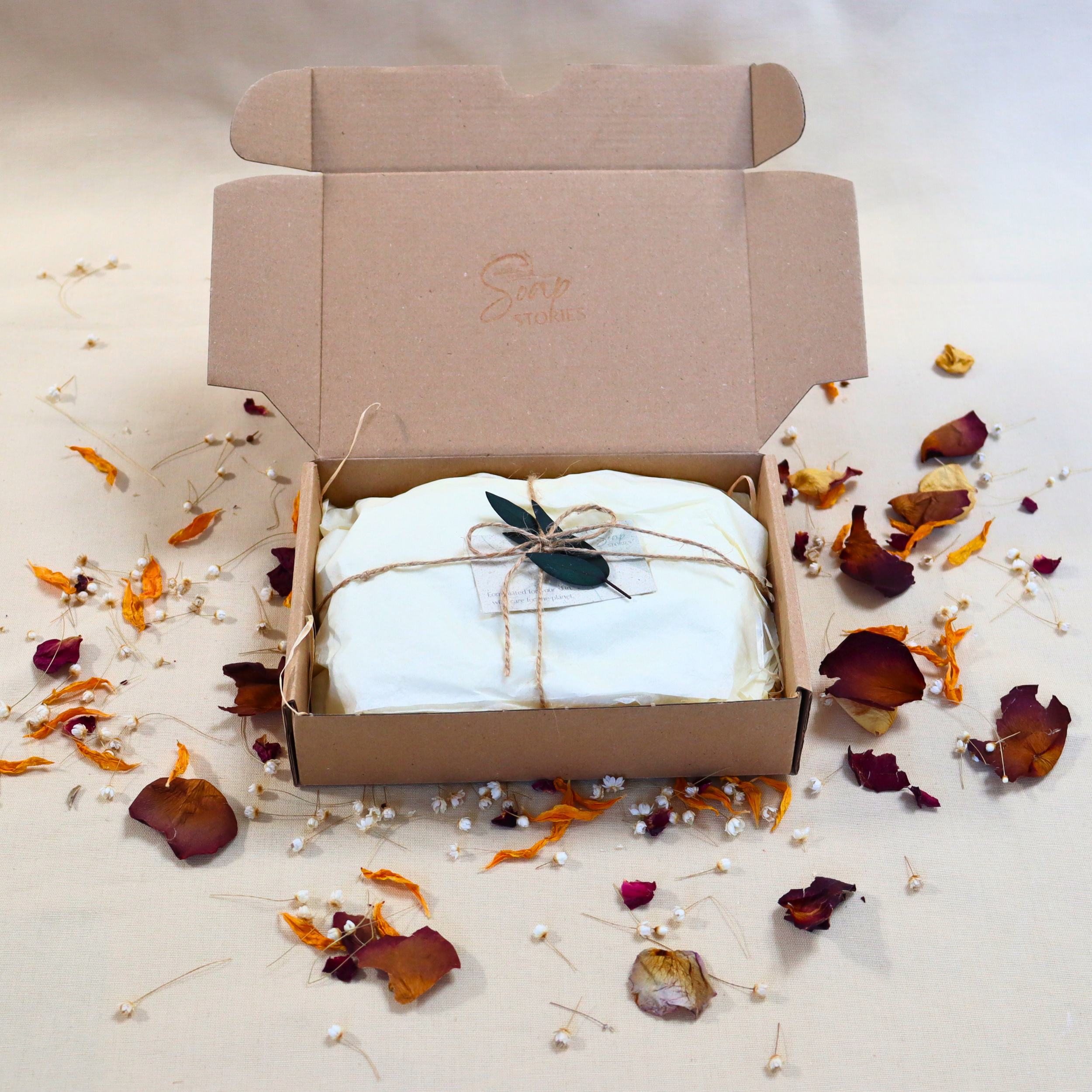 Eco-friendly gift box with handmade soaps wrapped in tissue and twine, decorated with dried flowers and leaves.