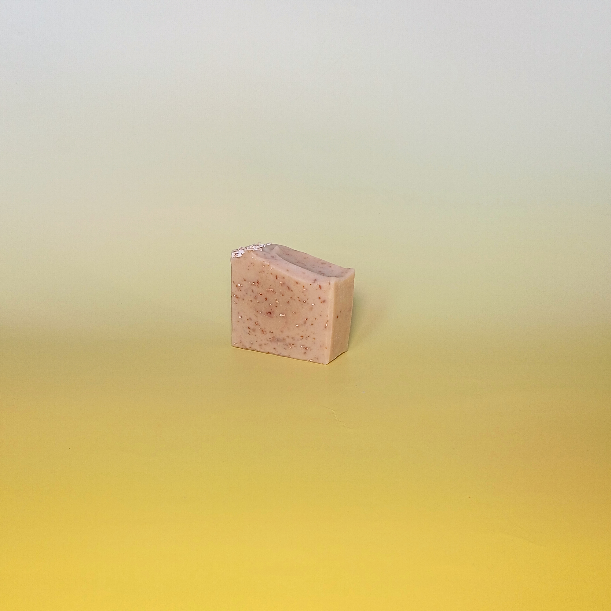 Handmade natural soap bar with a soft beige tone and visible oats, unscented and crafted with milk, honey, and oats, displayed on a pale yellow gradient background in a minimal composition.
