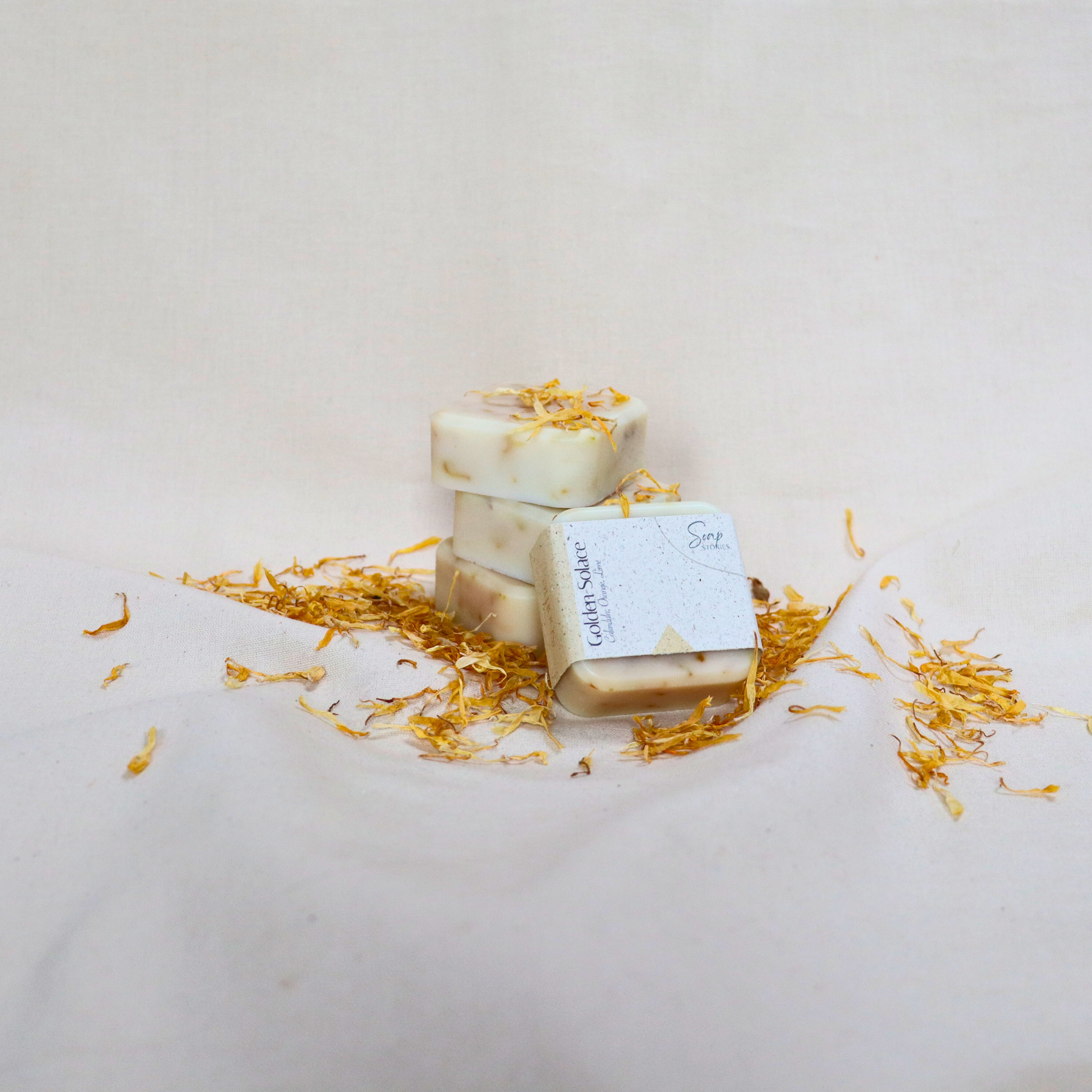 A stack of handmade calendula mini soaps with golden flower petals on a beige cloth background, showcasing a natural and soothing look.
