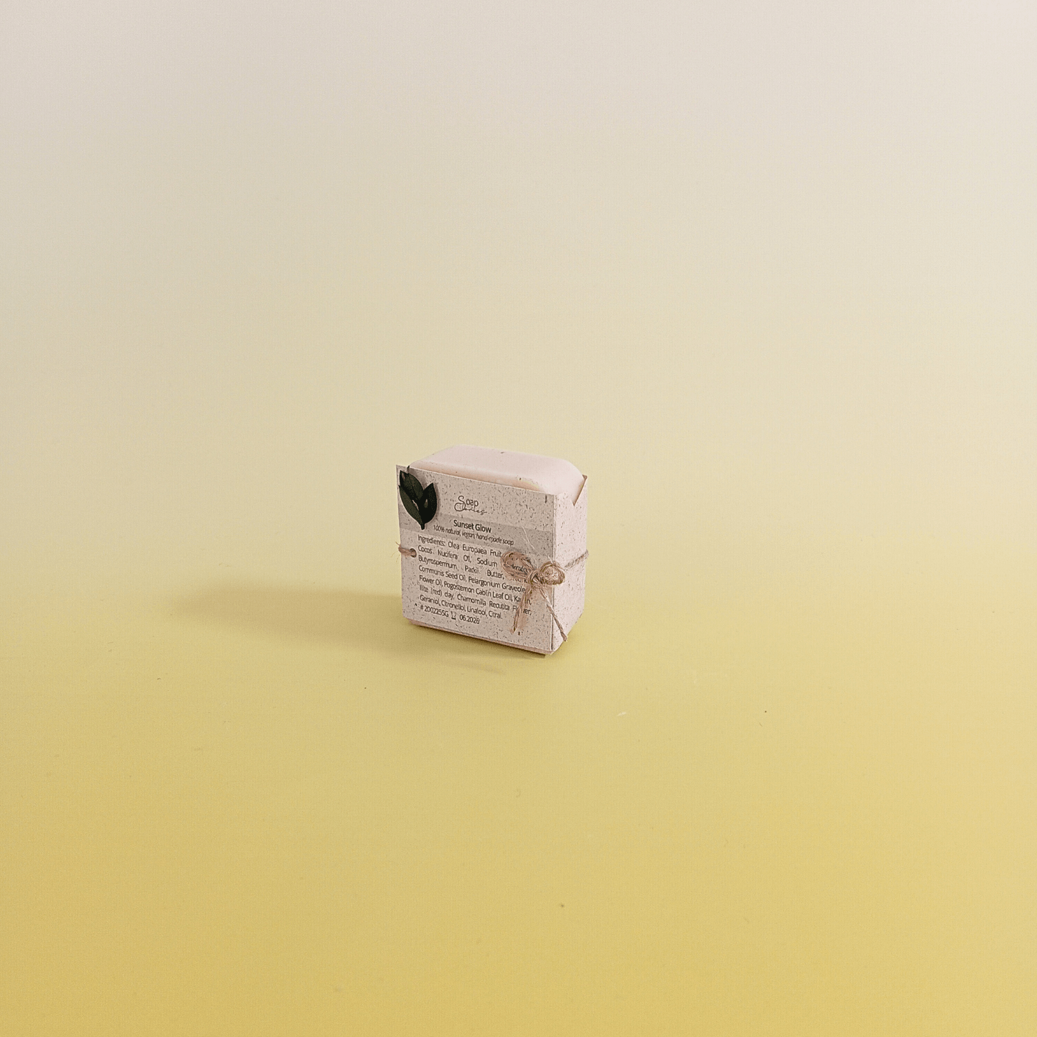 Natural soap bar wrapped in eco-friendly paper and tied with natural twine, displayed on a soft yellow gradient background, reflecting minimal and sustainable design.
