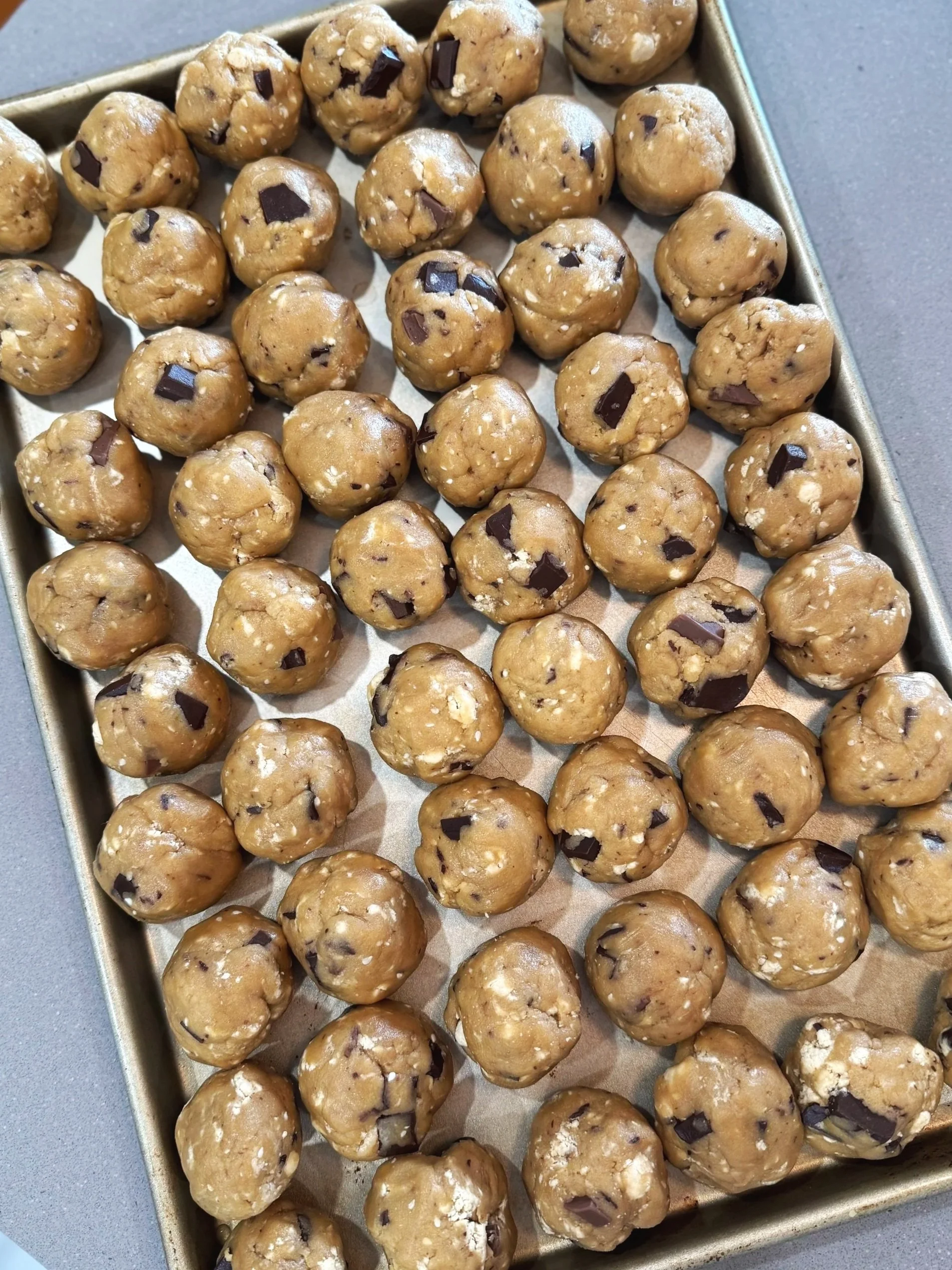 Batch of cookie dough balls with chocolate chunks on baking sheet.