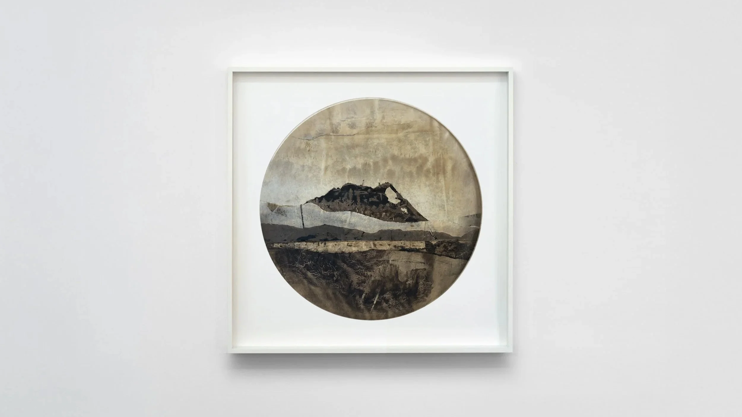 Art piece with a circular depiction of a mountain landscape in a white frame on a white wall.