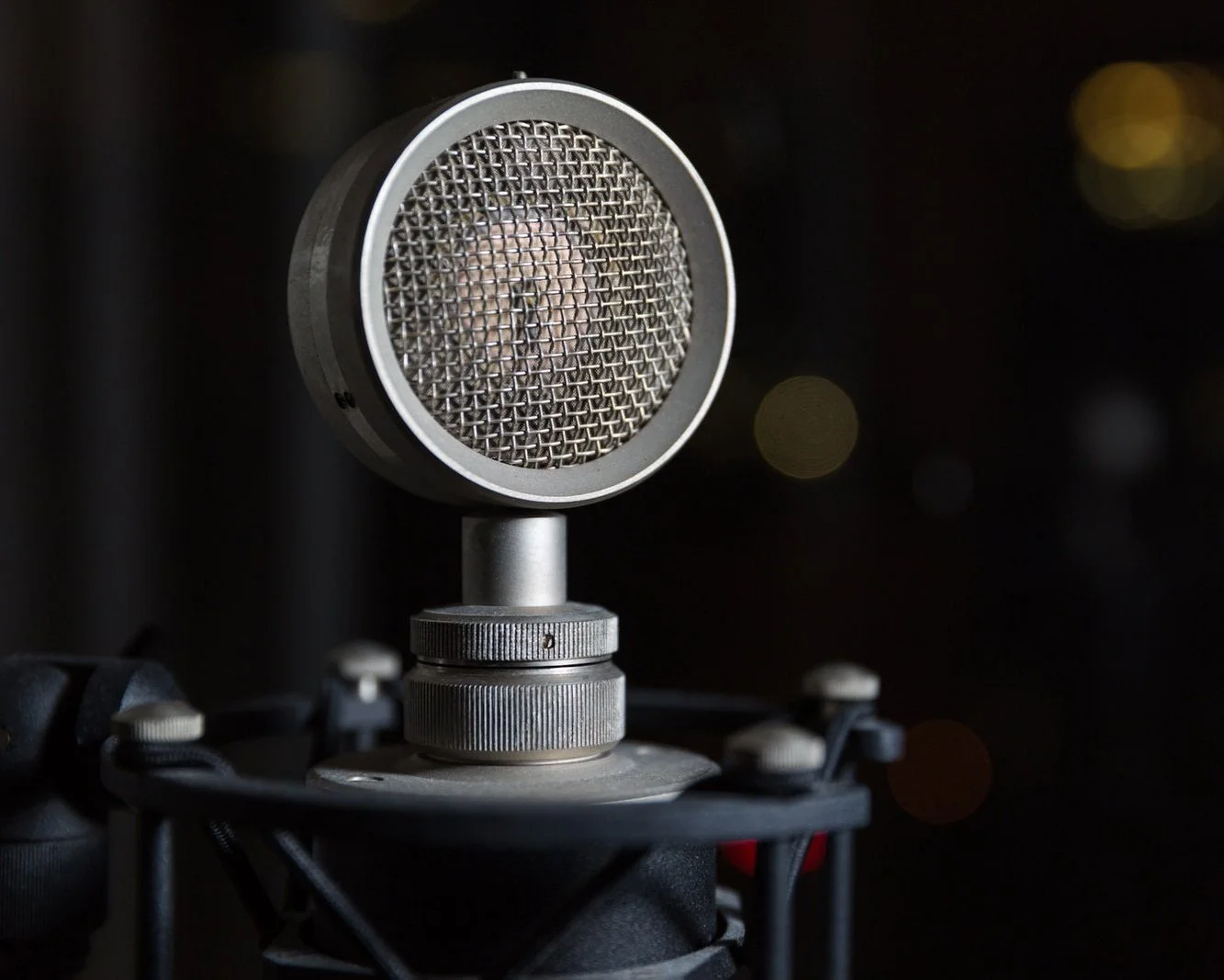 Close-up of a professional studio condenser microphone on a shock mount against a dark background.