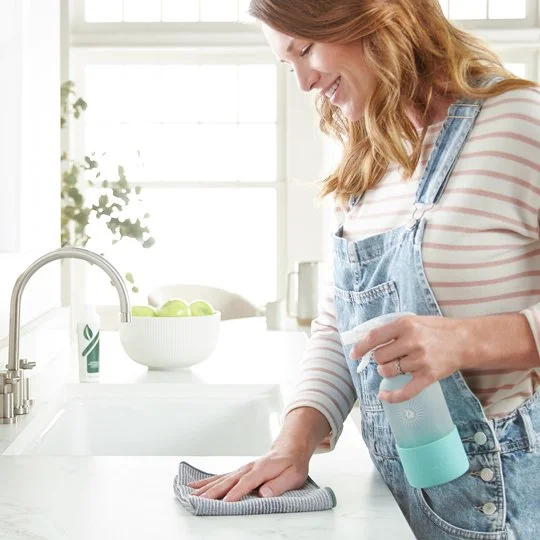 Woman cleaning a kitchen countertop with a spray bottle and cloth.
