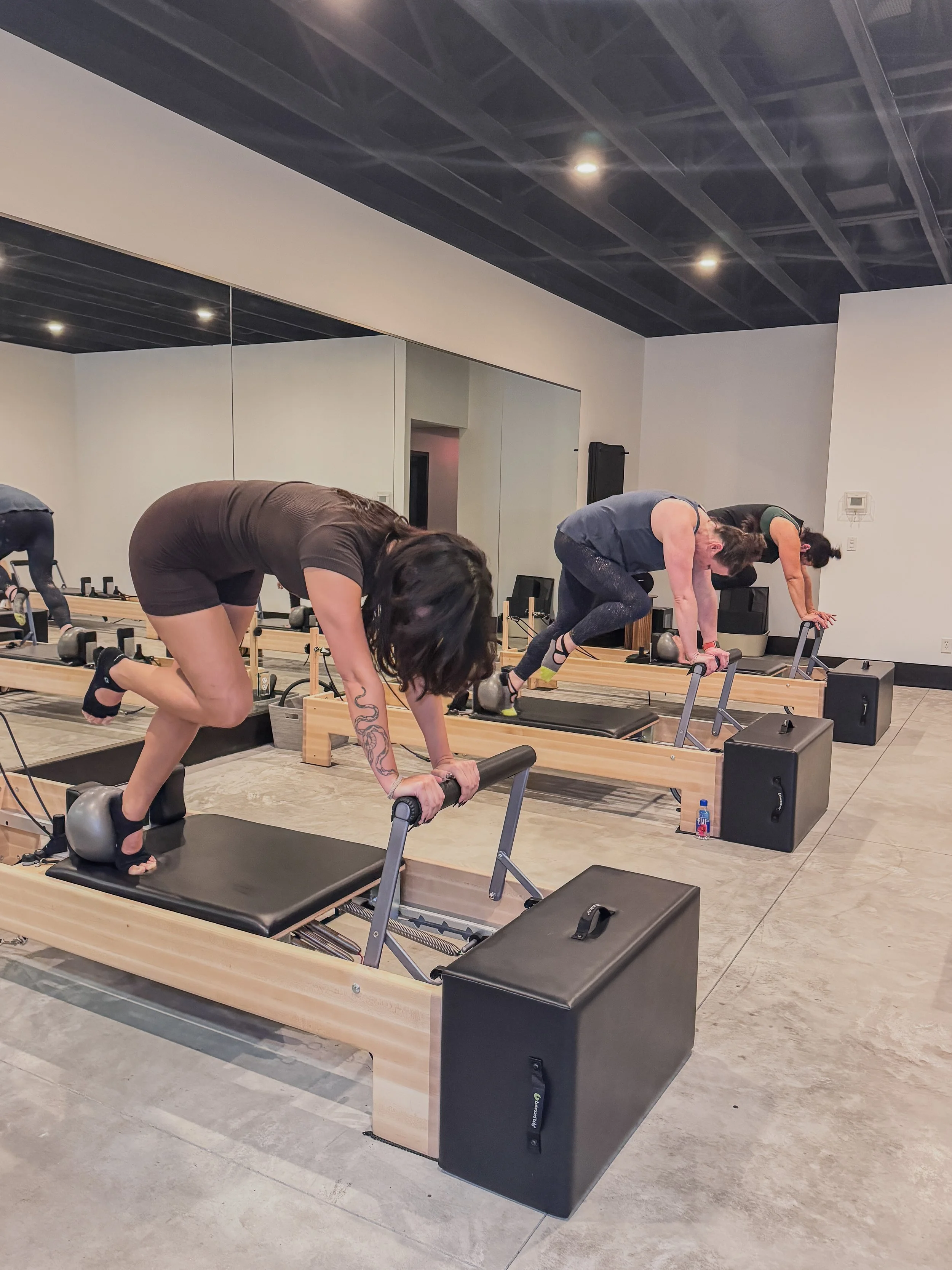 Three women doing Pilates on reformer machines in a fitness studio.