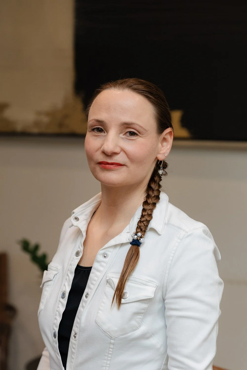 A massage therapist with long dark hair and glasses, wearing a blue sweater, standing in front of a dark wooden background.