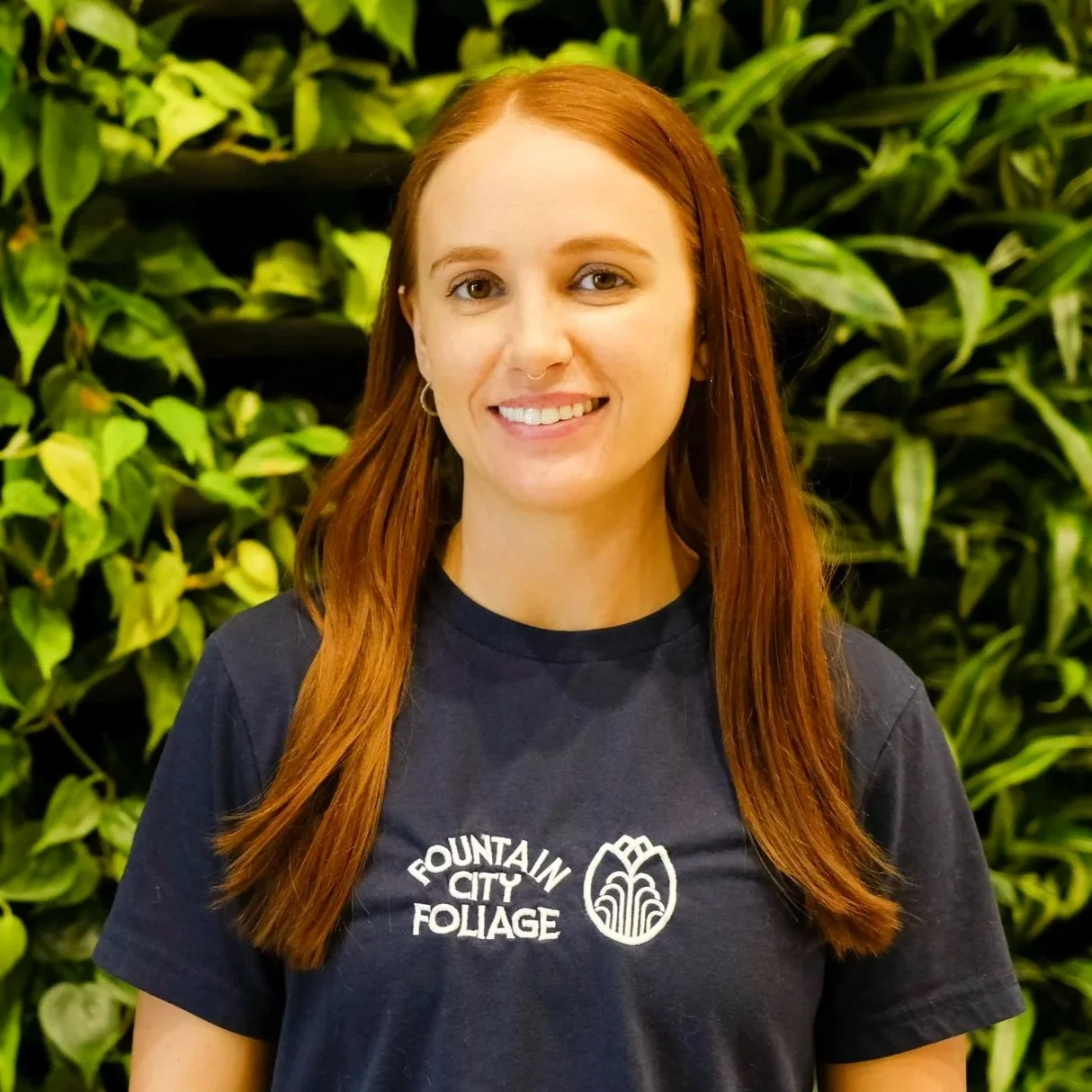 The owner of Fountain City Foliage is pictured in front of a living green plant wall in Overland Park, Kansas, near downtown Kansas City. She provides interior landscaping services to the Kansas City Metro area