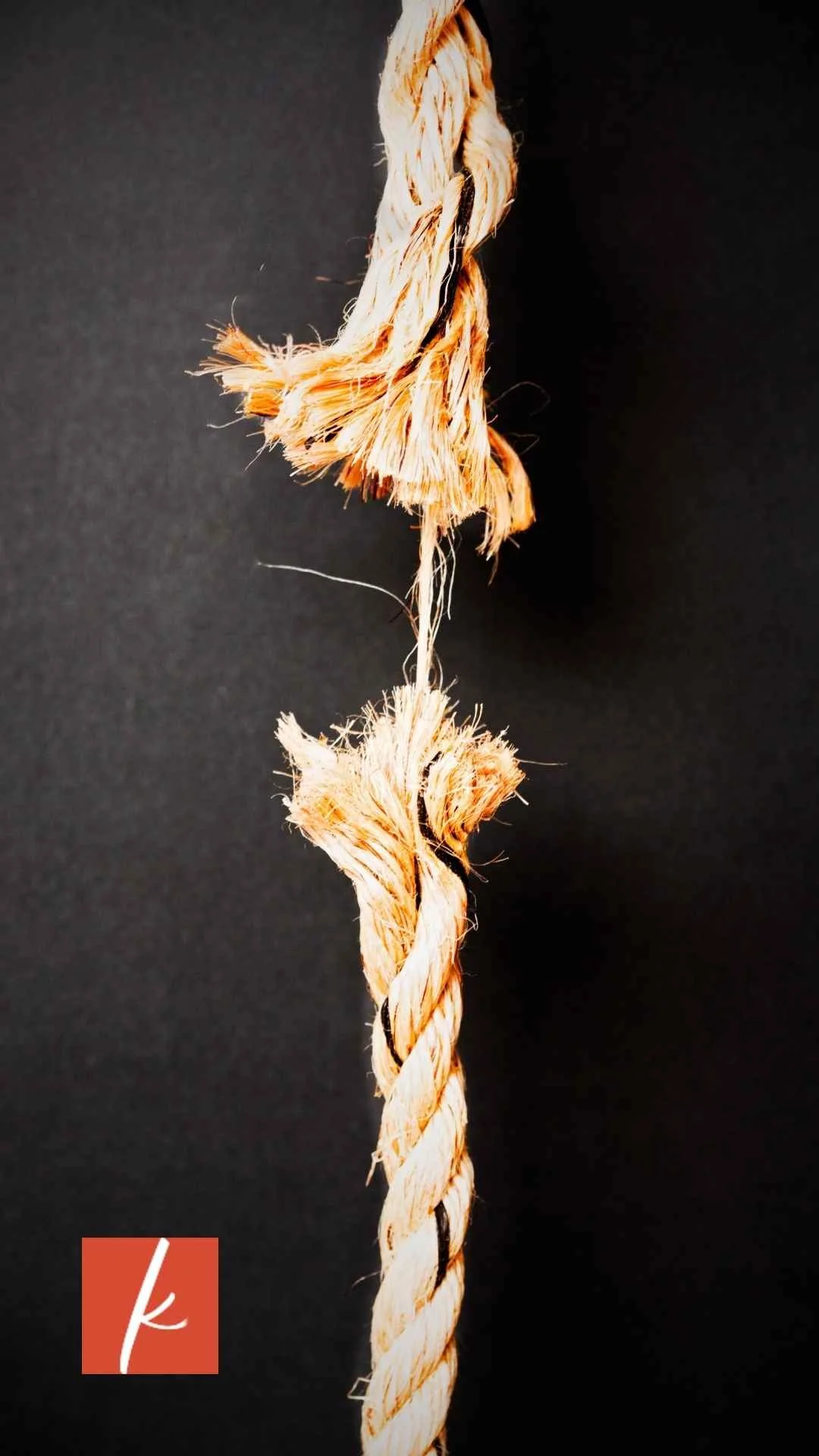 Close-up view of a broken rope with frayed ends on a black background.