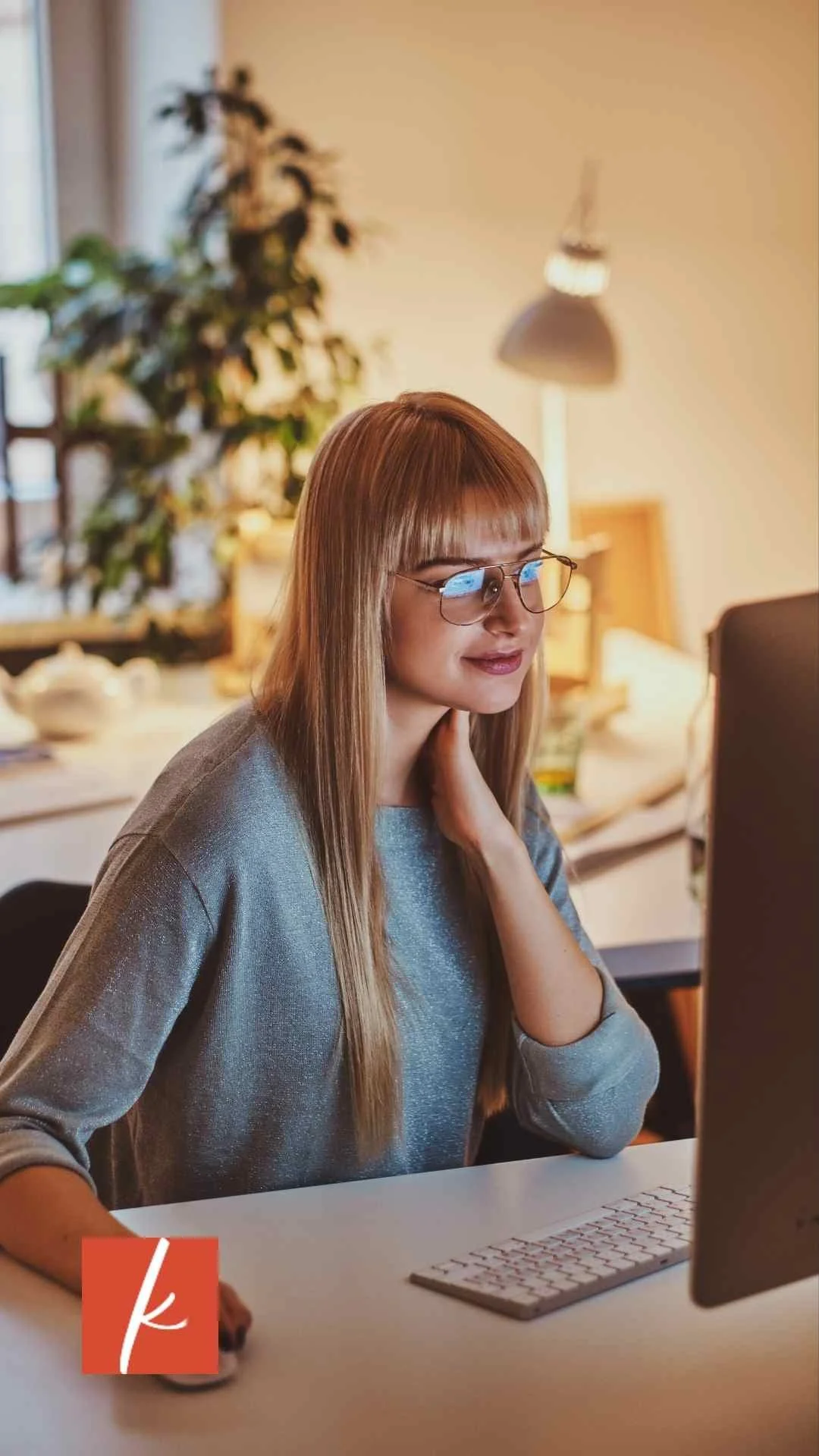 A woman with glasses sitting at a desk and looking at a computer screen