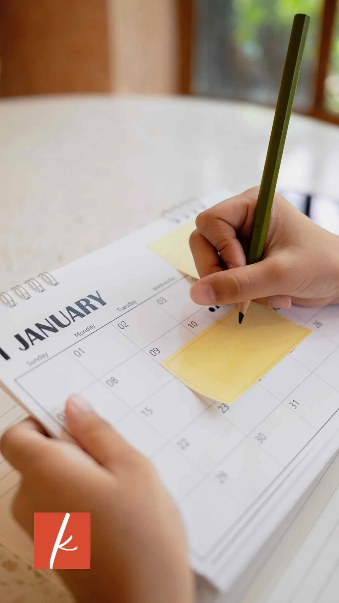 January calendar with a yellow sticky note and a hand holding a pencil.