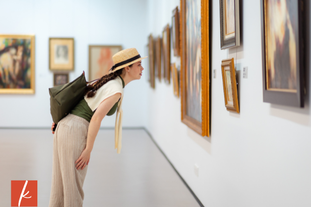 women with brown hair in braids leaned over looking at a painting in a art gallery