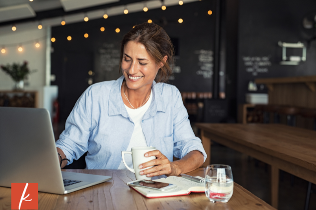 Woman at a cafe with laptop and coffee smiling