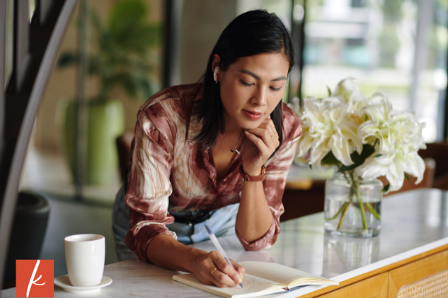 Woman leaning on counter writing in journal with cup of coffee