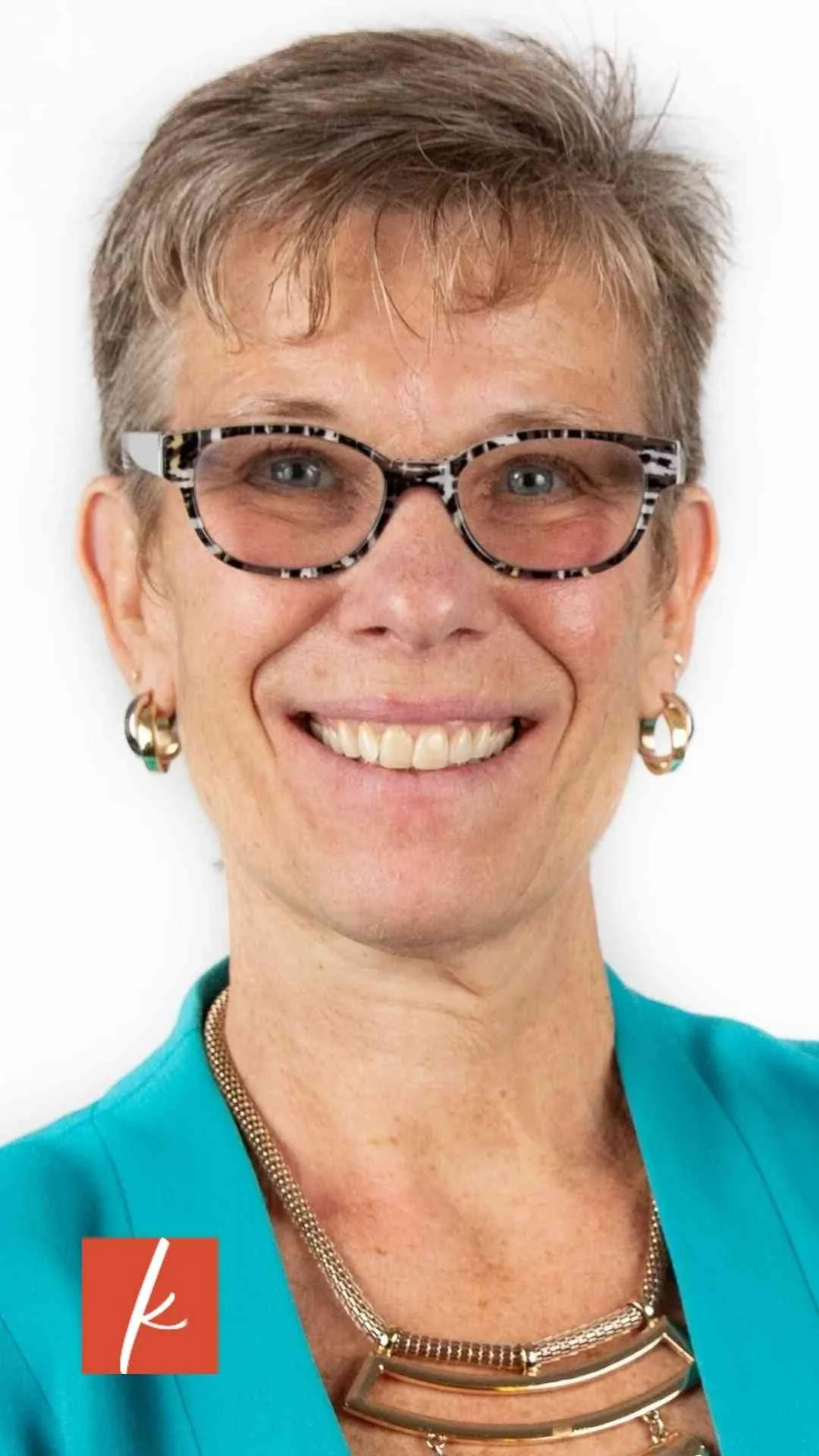 Smiling woman with short gray hair wearing glasses and a teal blazer.