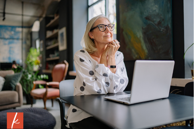 Woman sitting at a table in front of her laptop looking up and daydreaming