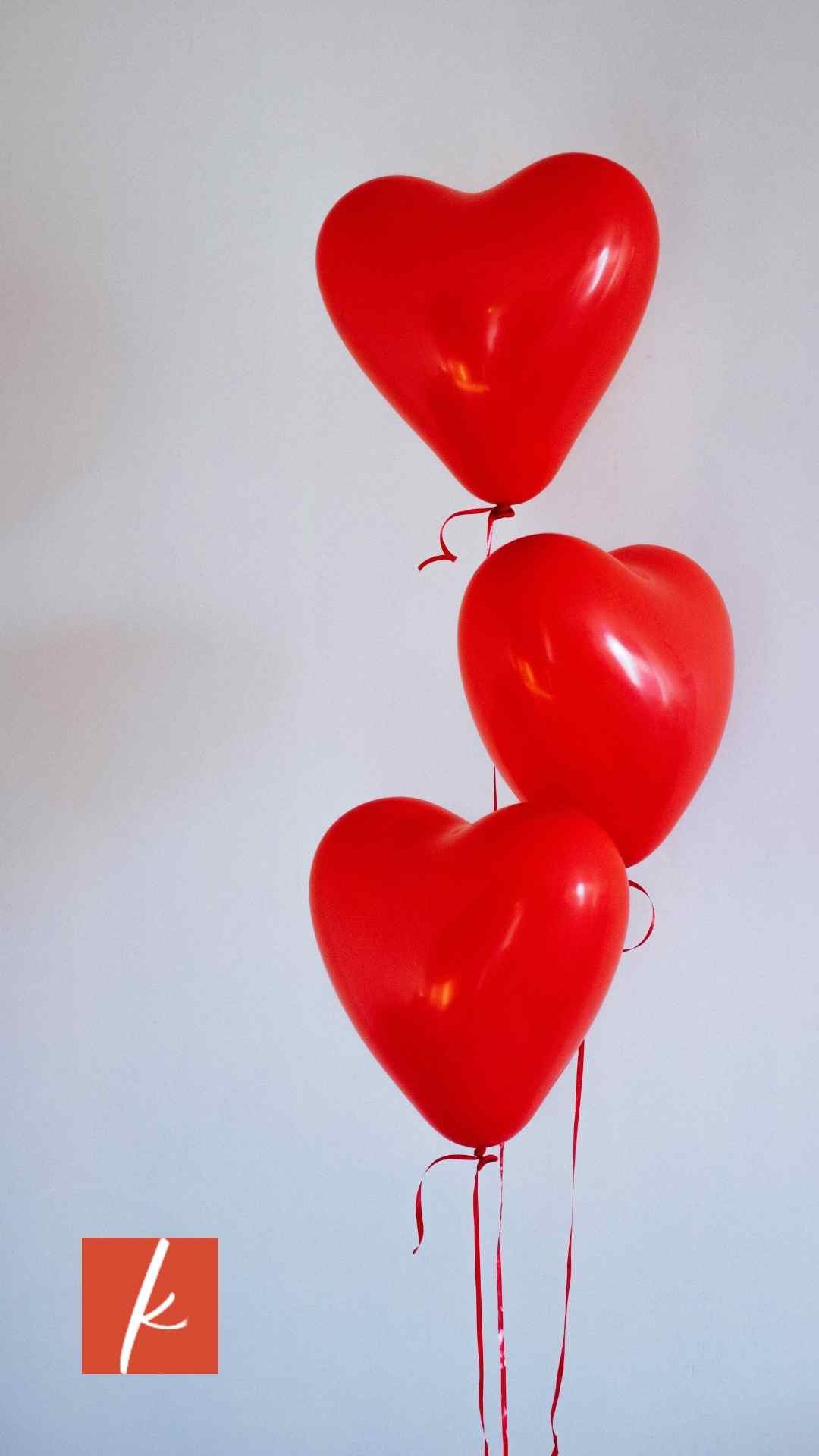 Three red balloons in the shape of hearts with read string on a grey background.