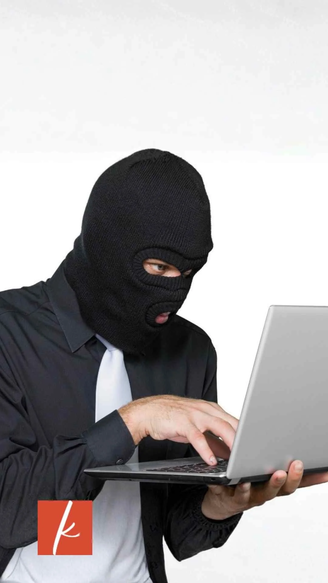 Person wearing a black face covering and business attire typing on a laptop.