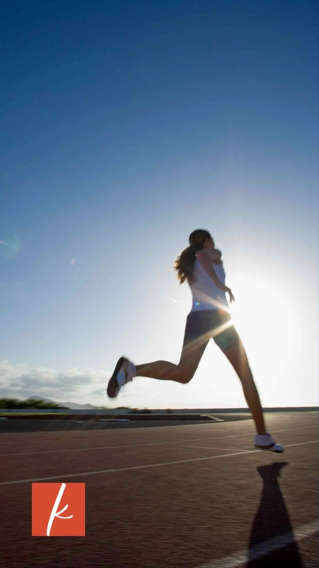 A woman running on a track outdoors with the sun low in the sky.