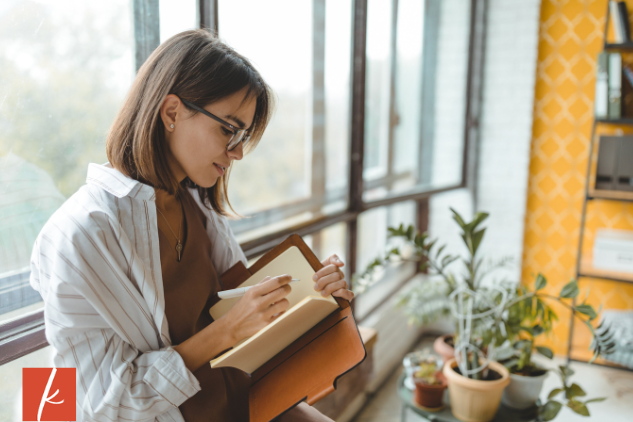 Woman writing in a journal sitting on window ledge