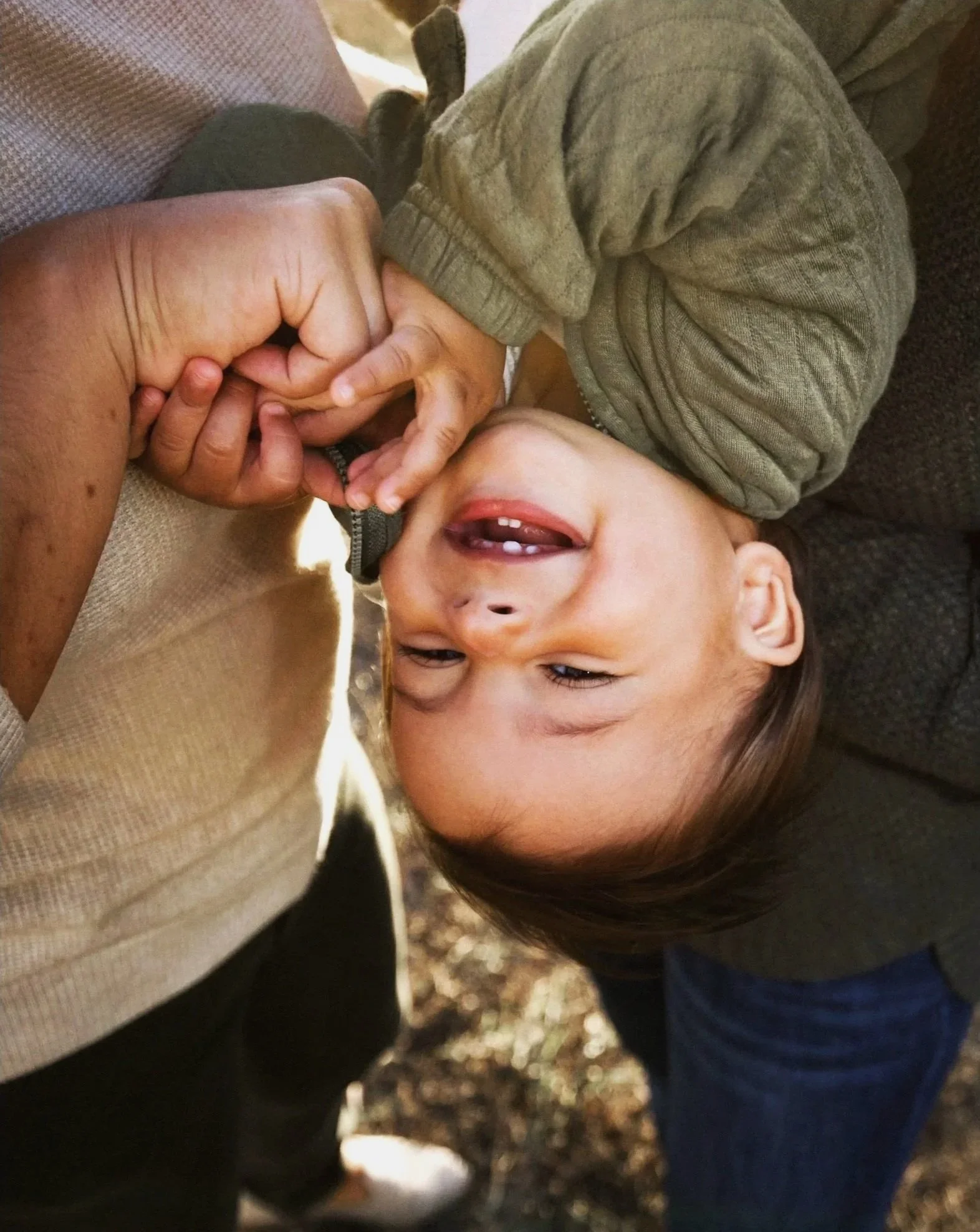 A young child with brown hair, smiling, holding hands with his parents, upside down and being silly in the photo. Family photos in Northlake, TX.