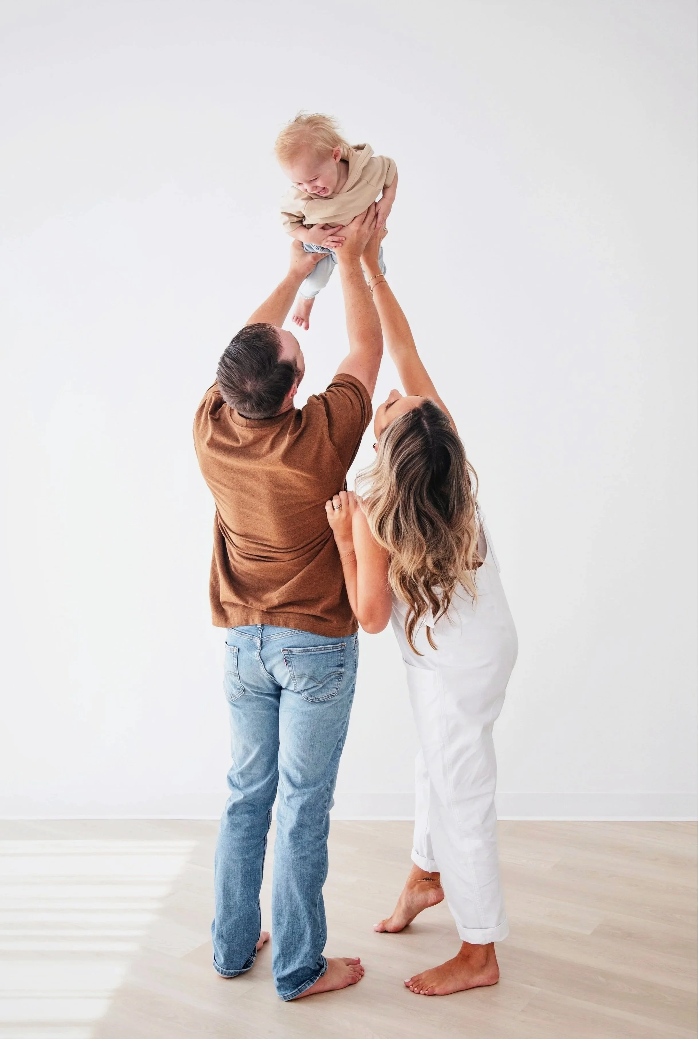 Two adults holding a baby in the air, against a white background. North Texas family photographer indoor studio session.