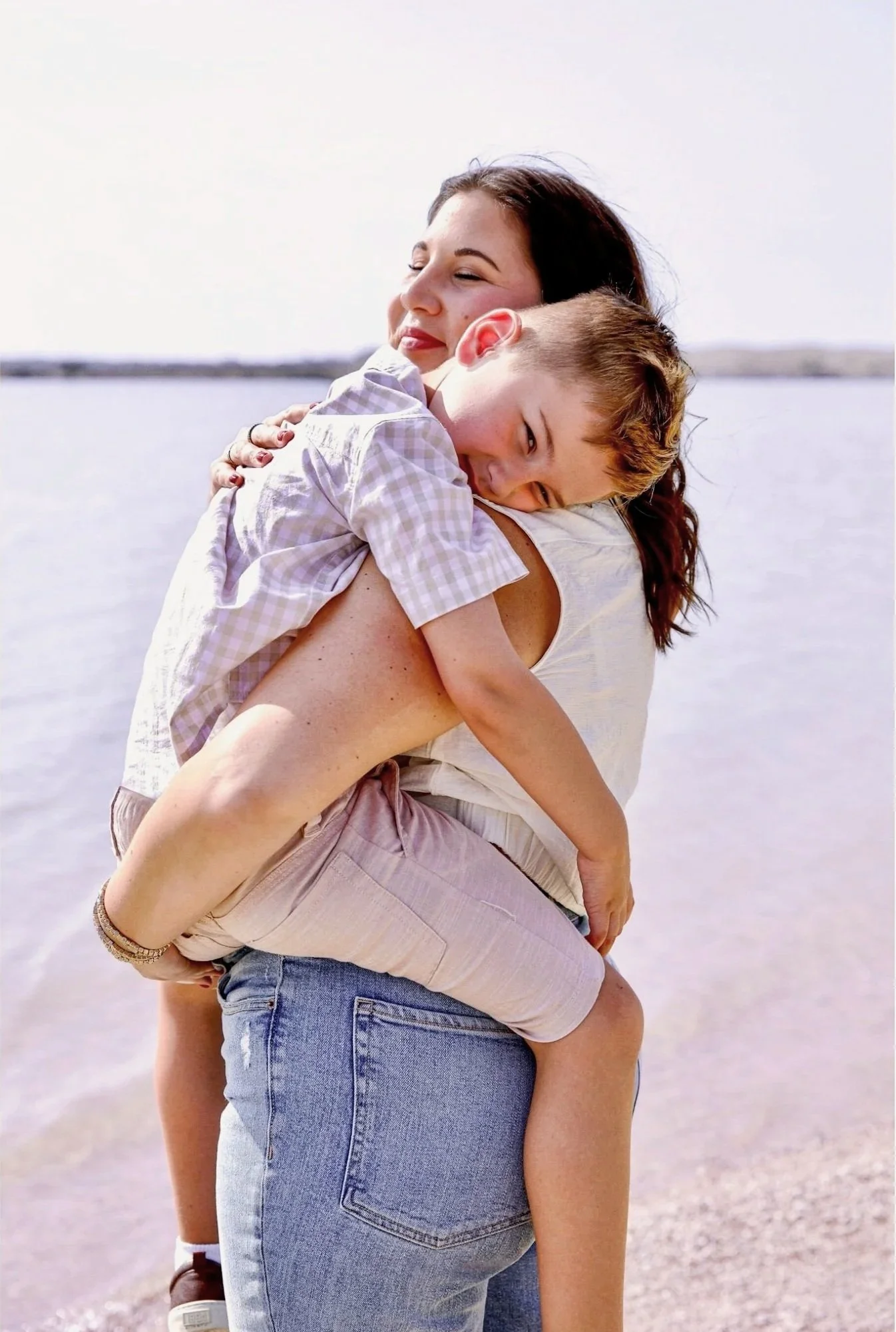A person holding a child near a body of water on a sunny day, both smiling and hugging closely. North Texas family photographer outdoor mommy and me session.