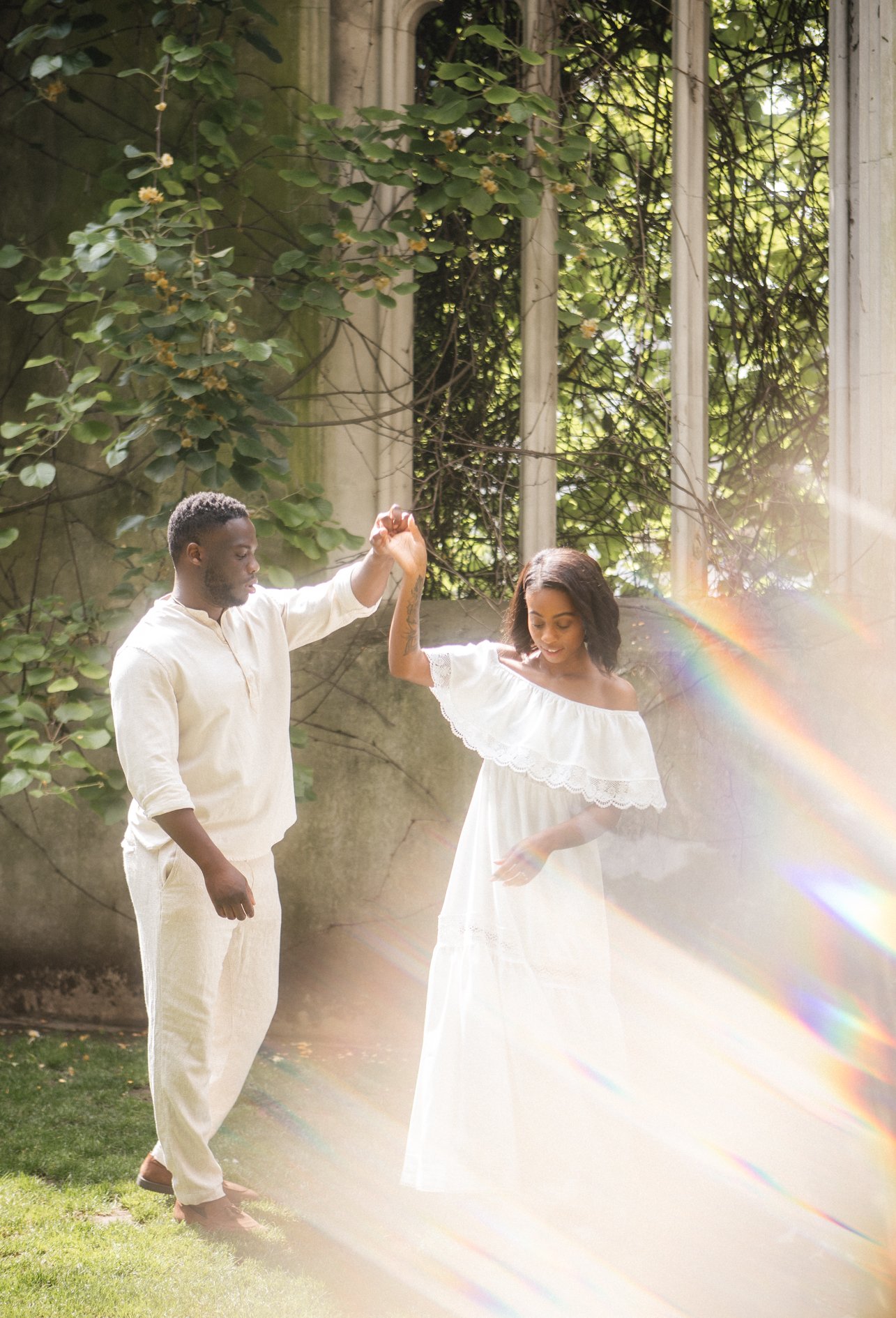 A couple dancing outdoors in the sunlight at st dunstan in the east, with a rainbow lens flare and greenery background.