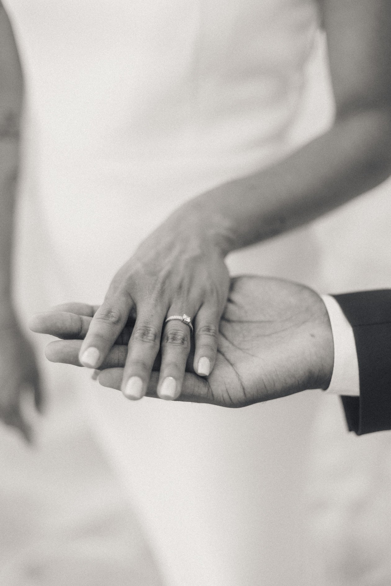 Close-up of a hand wearing a wedding ring, touching another person's hand at a wedding or engagement ceremony.