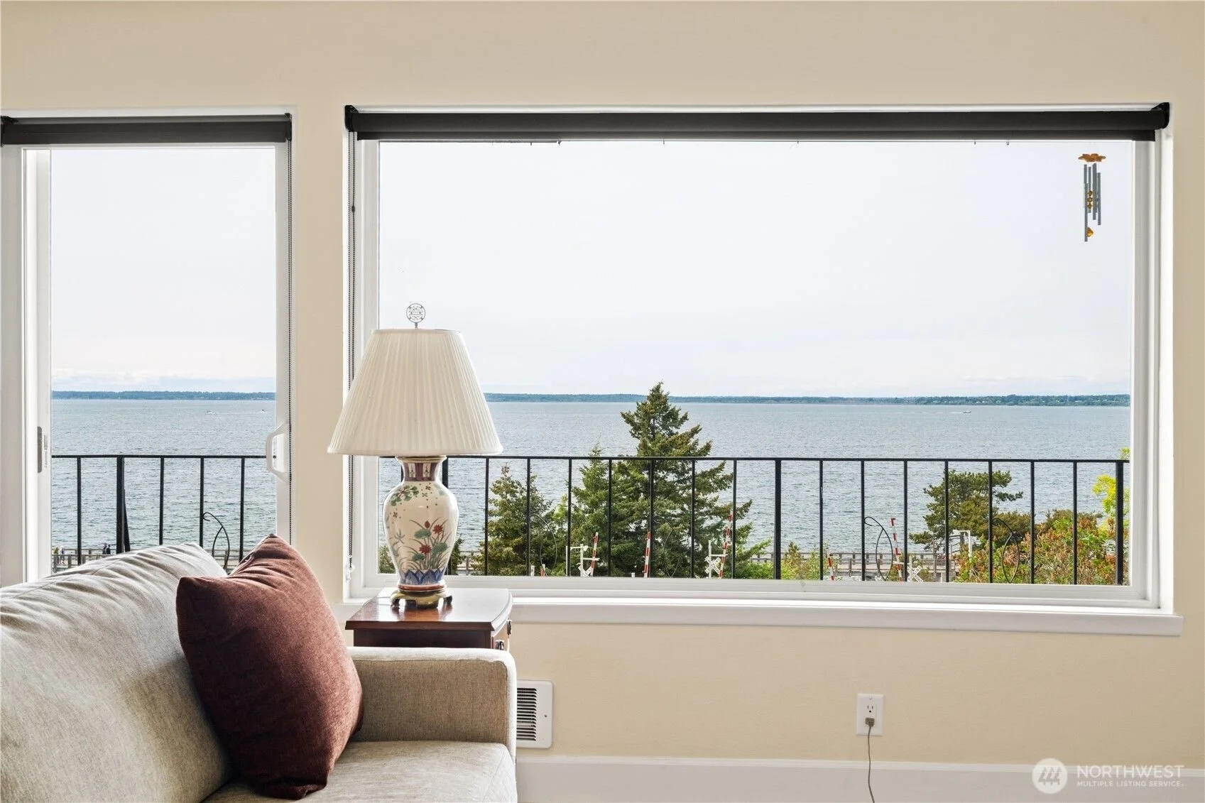 Living room with large window overlooking a body of water and trees, beige sofa with brown pillow, lamp on side table near window in Bellingham WA