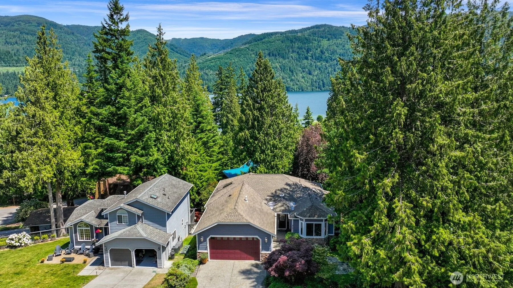Aerial view of a house surrounded by tall trees near a lake, with hills and mountains in the background in Bellingham WA